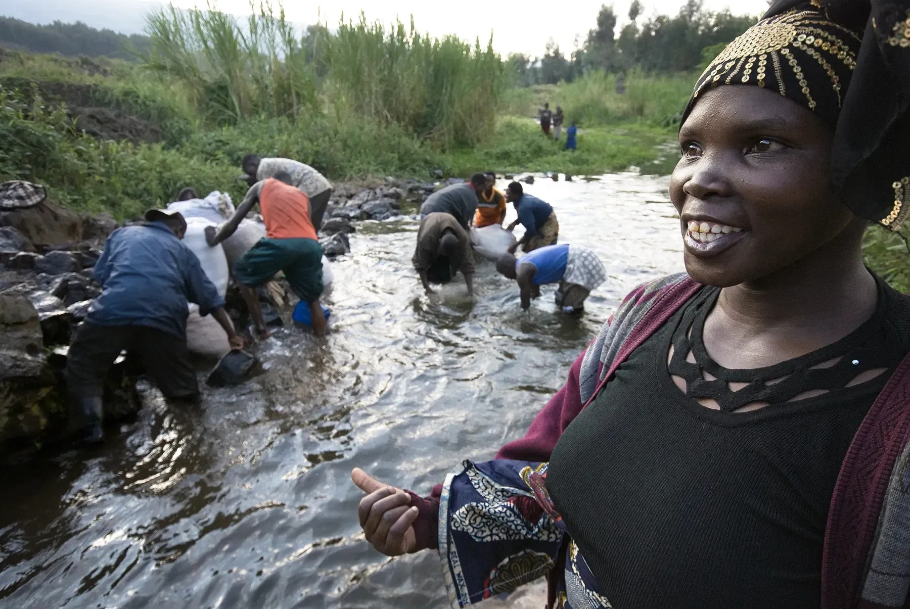 Group of people collecting water from a river, with a smiling woman in the foreground.