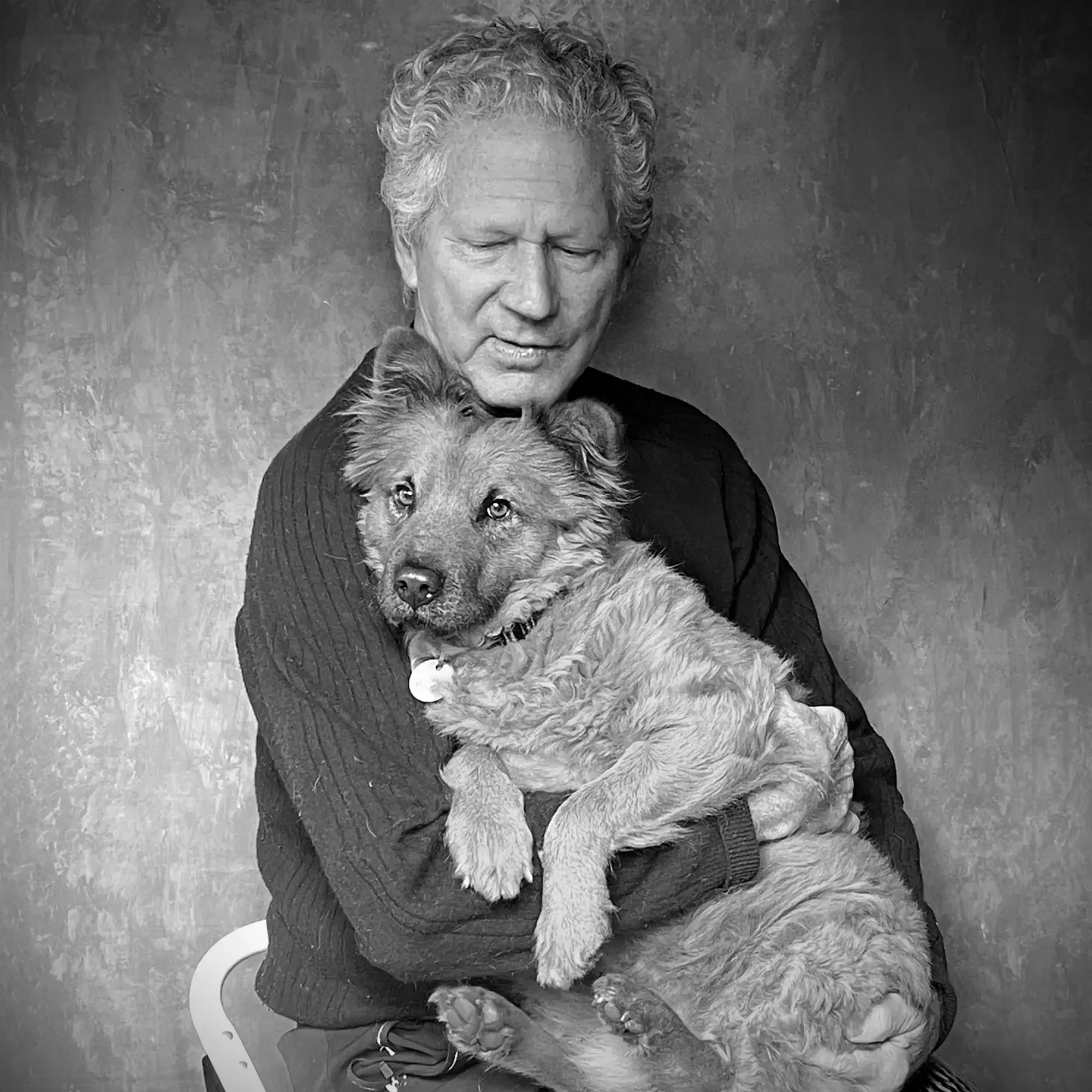 A black and white photo of an elderly man holding a young puppy in his arms, both looking at the camera.