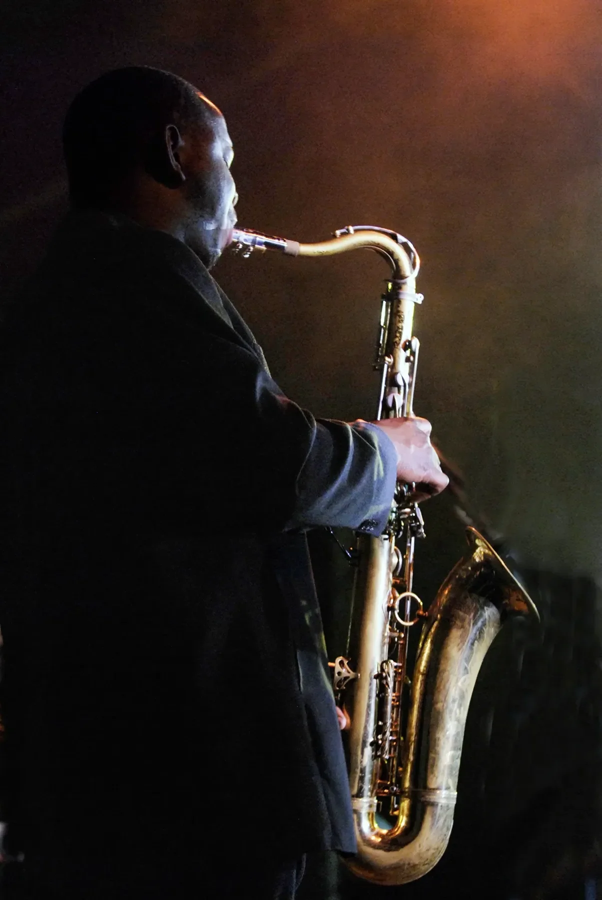 A person playing a saxophone in a dimly lit setting with a dark background.