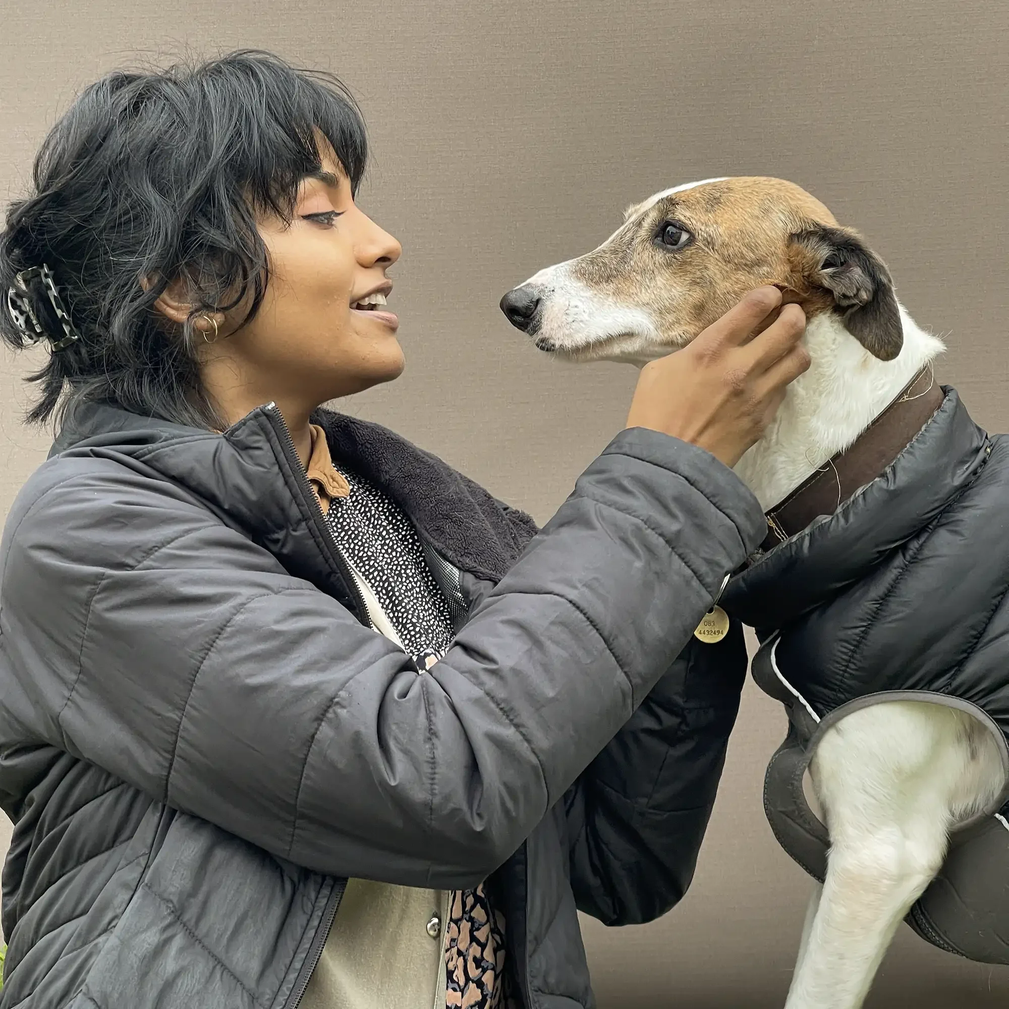 A woman gently holding a dog's face and smiling.