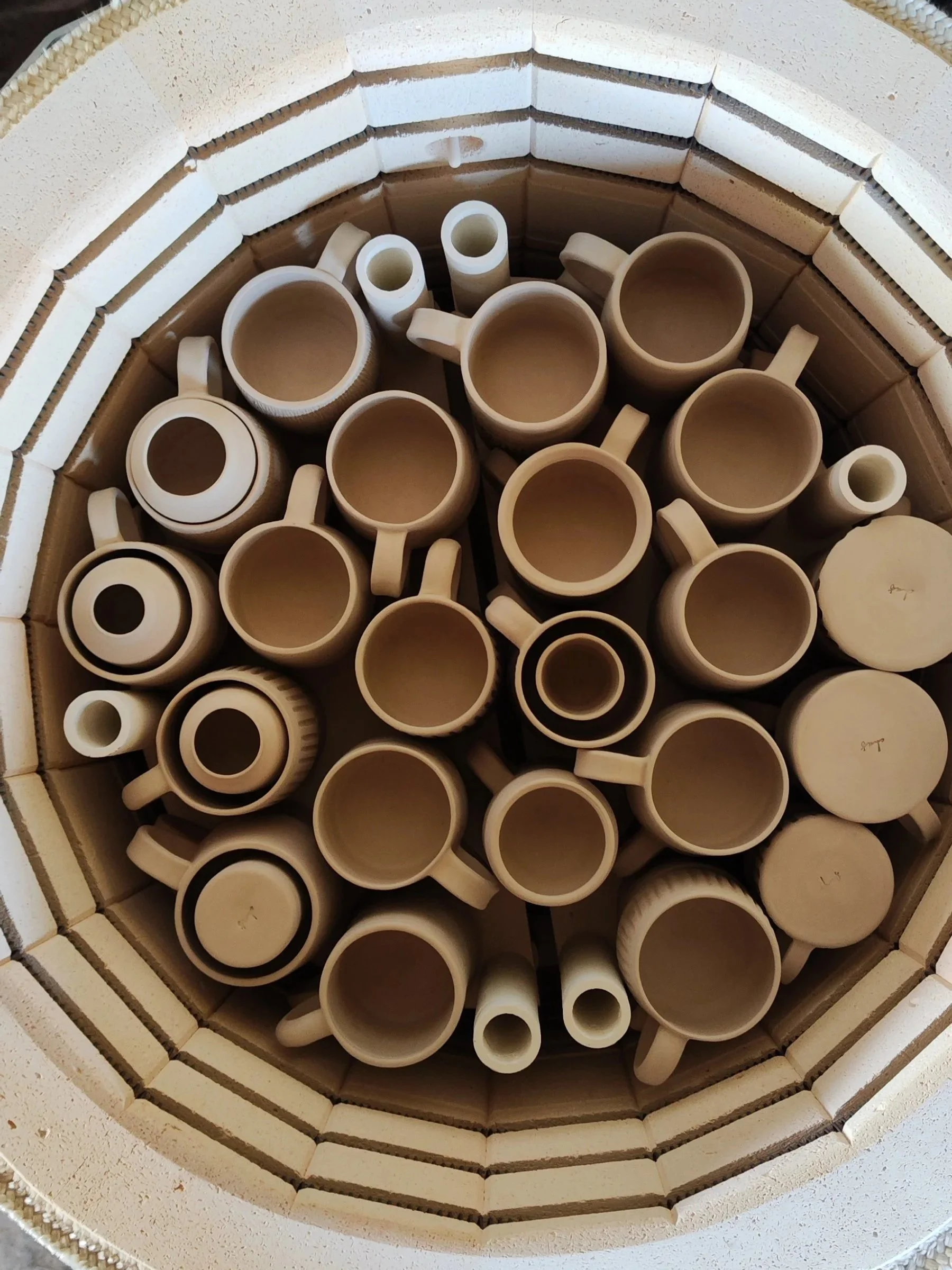 Top view of a kilncontaining various sizes of ceramic cups and mugs arranged in a circular pattern.