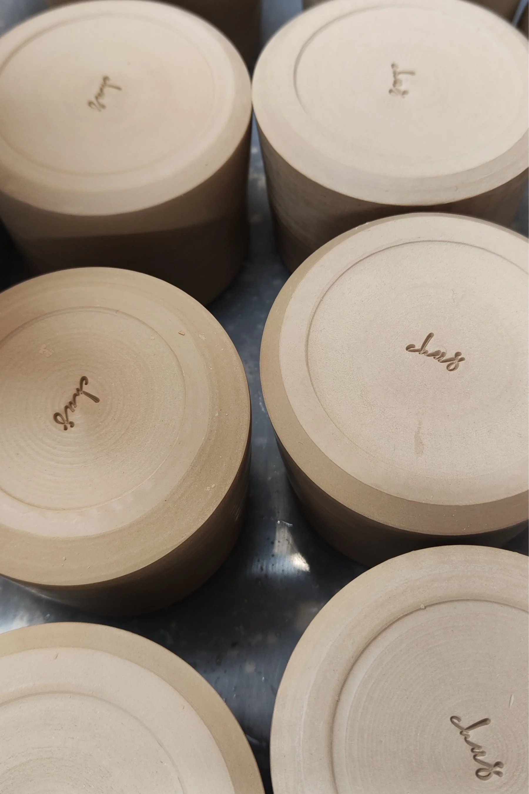 Close-up image of the bottom of several pots, with some logs having the words "Chus" written on the bottom. 