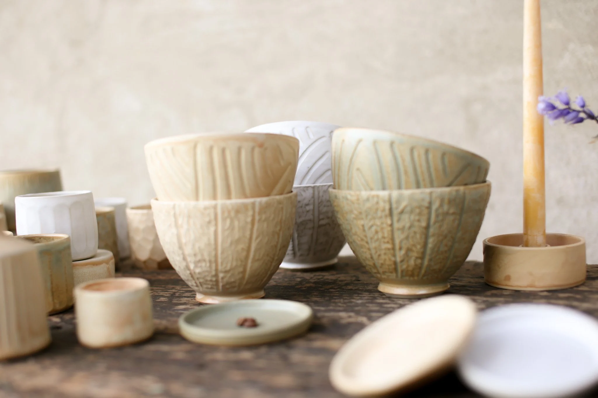 Various handmade ceramic bowls and cups in neutral tones on a wooden surface with a blurred background.