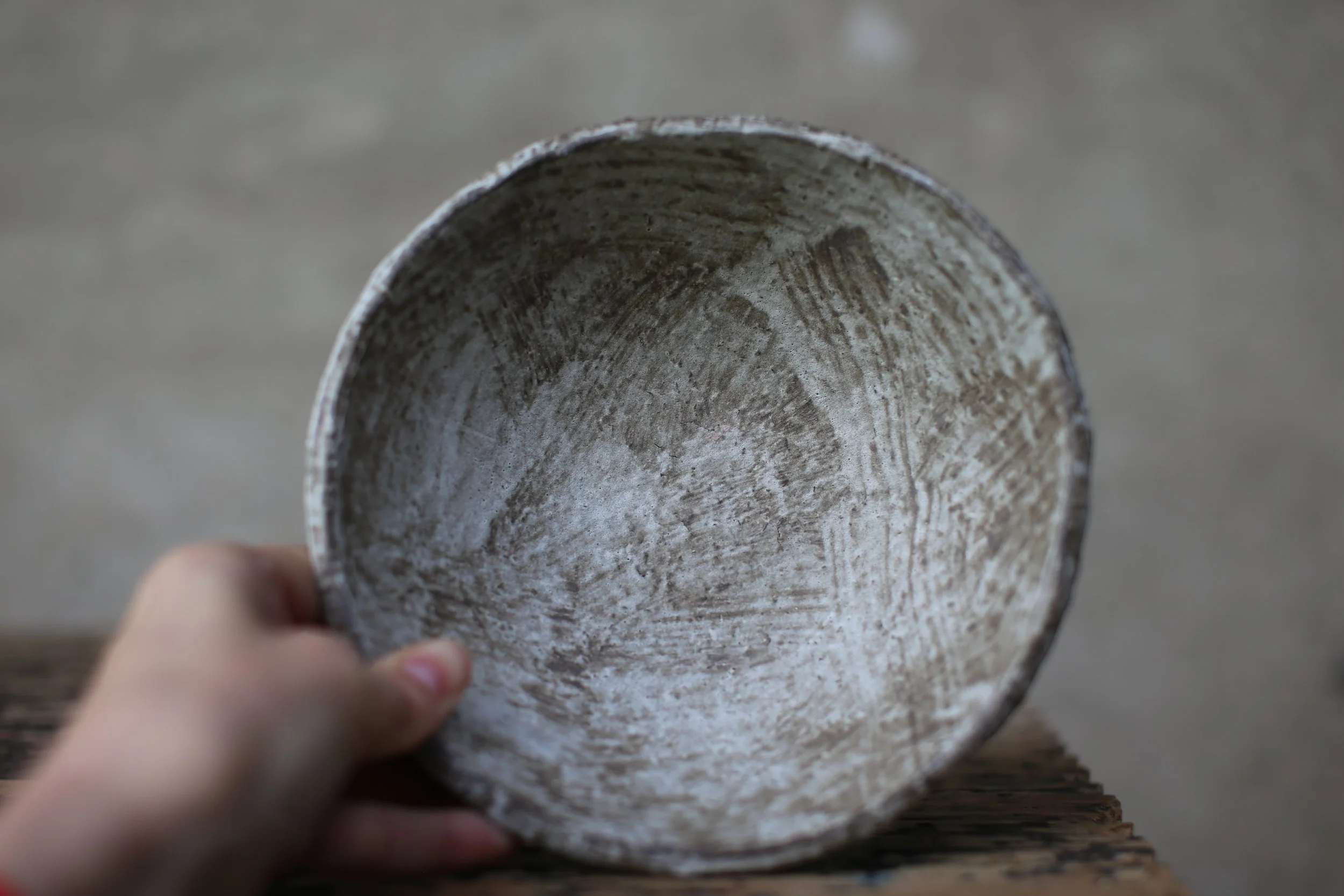 Close-up of the inside of a rustic bowl held by a person's hand, showing a textured interior on a wooden surface.