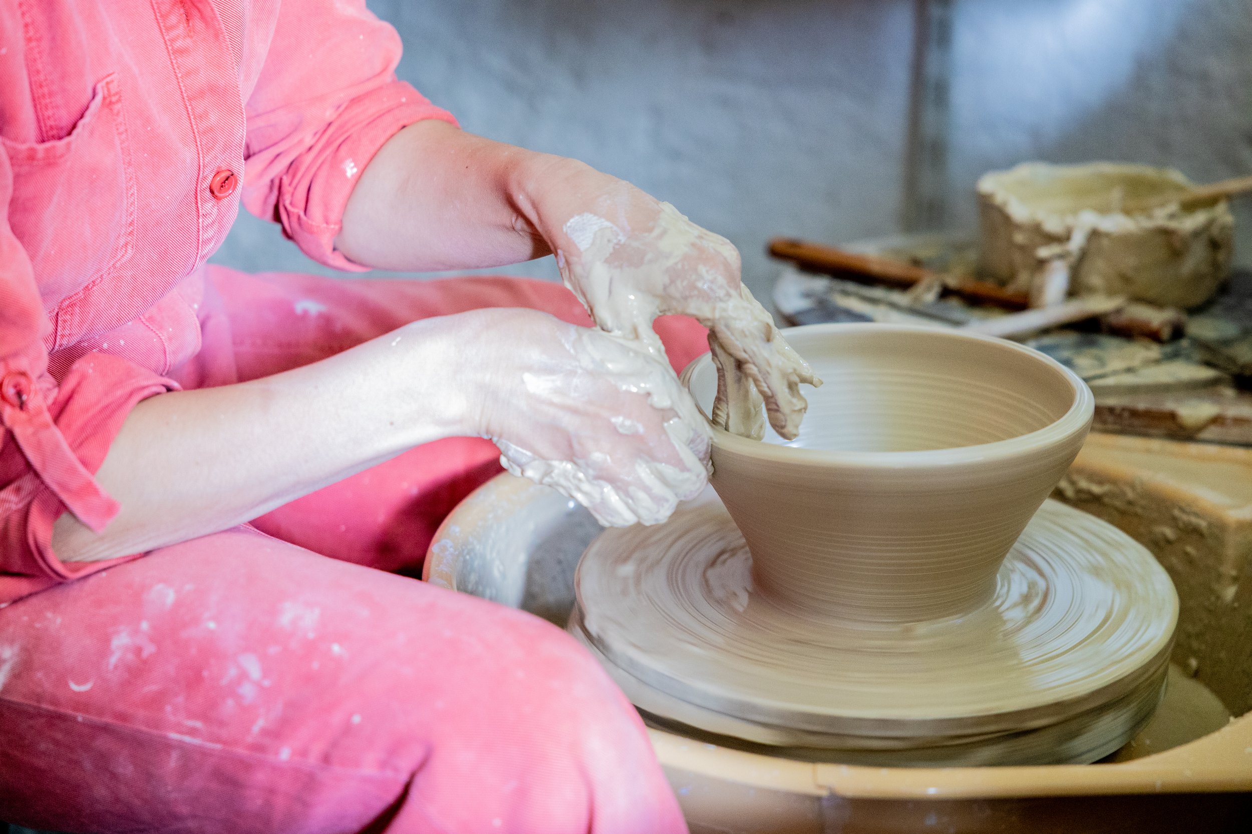 A person in a pink shirt and pink apron shaping clay on a pottery wheel.
