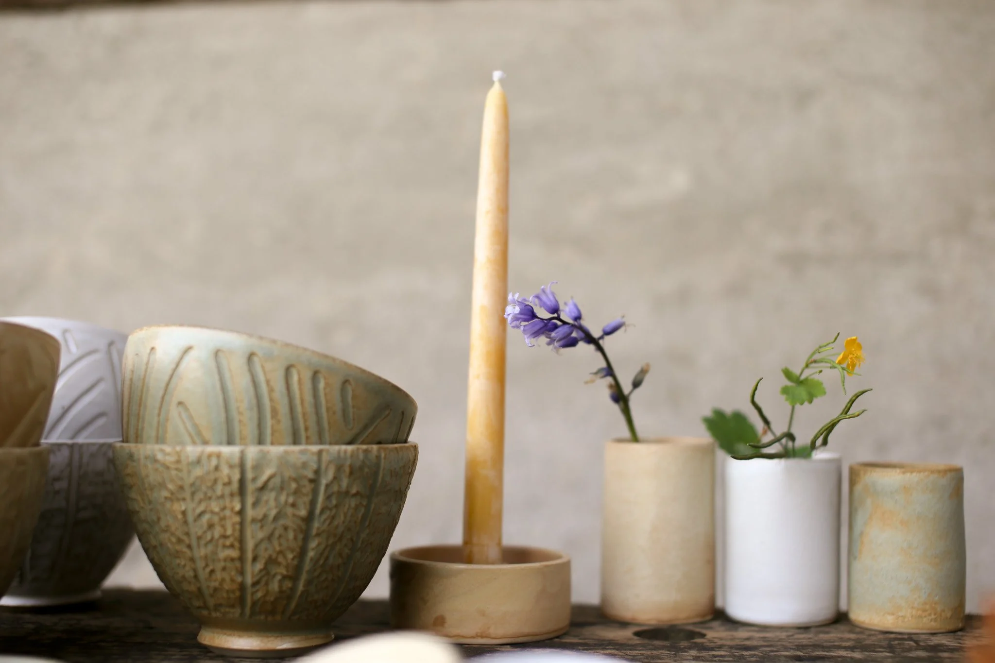 Collection of ceramic bowls and vases with flowers on display against a neutral background.