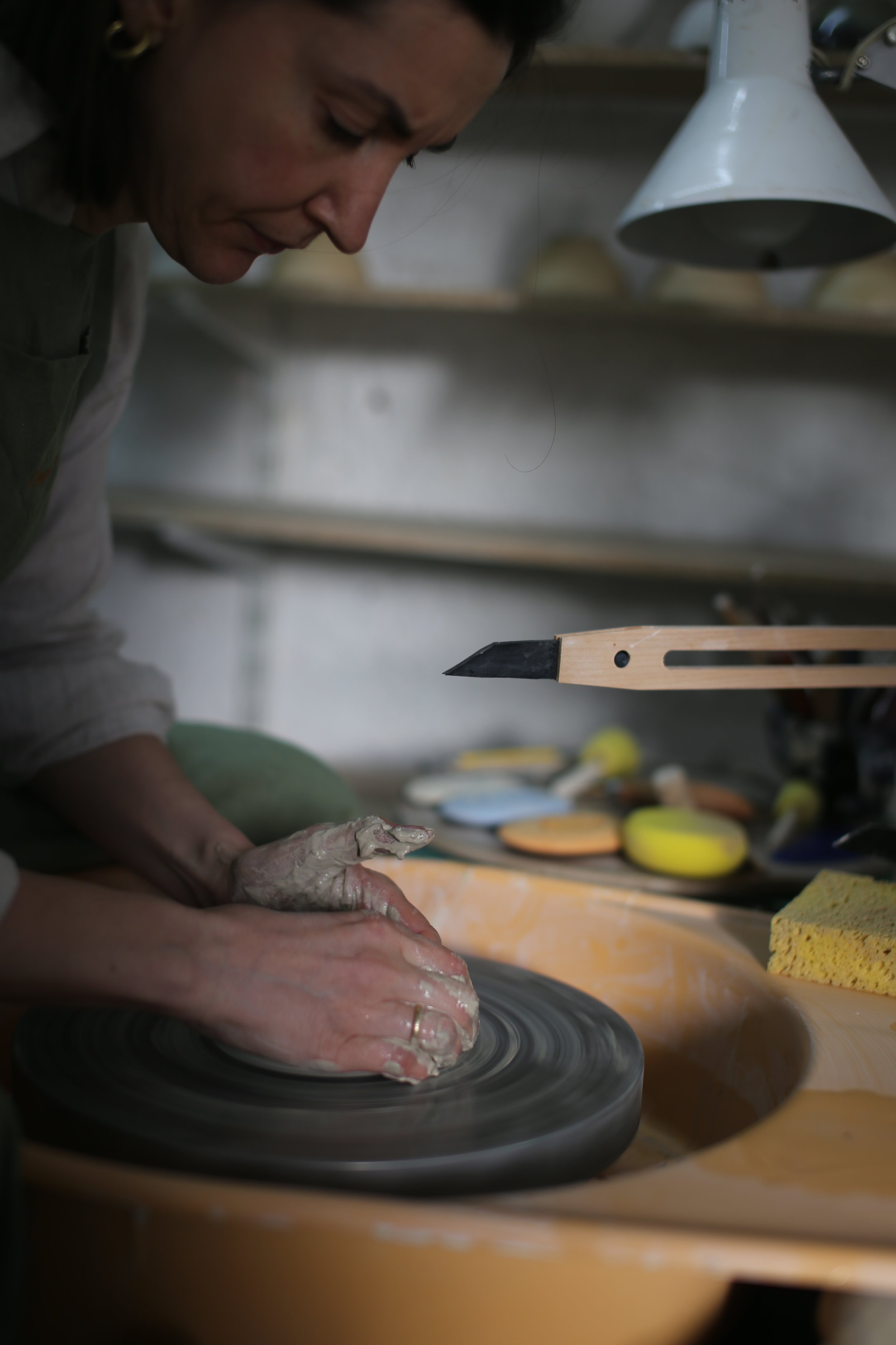 Person shaping clay on a pottery wheel in a studio surrounded by various pottery tools and finished pieces.