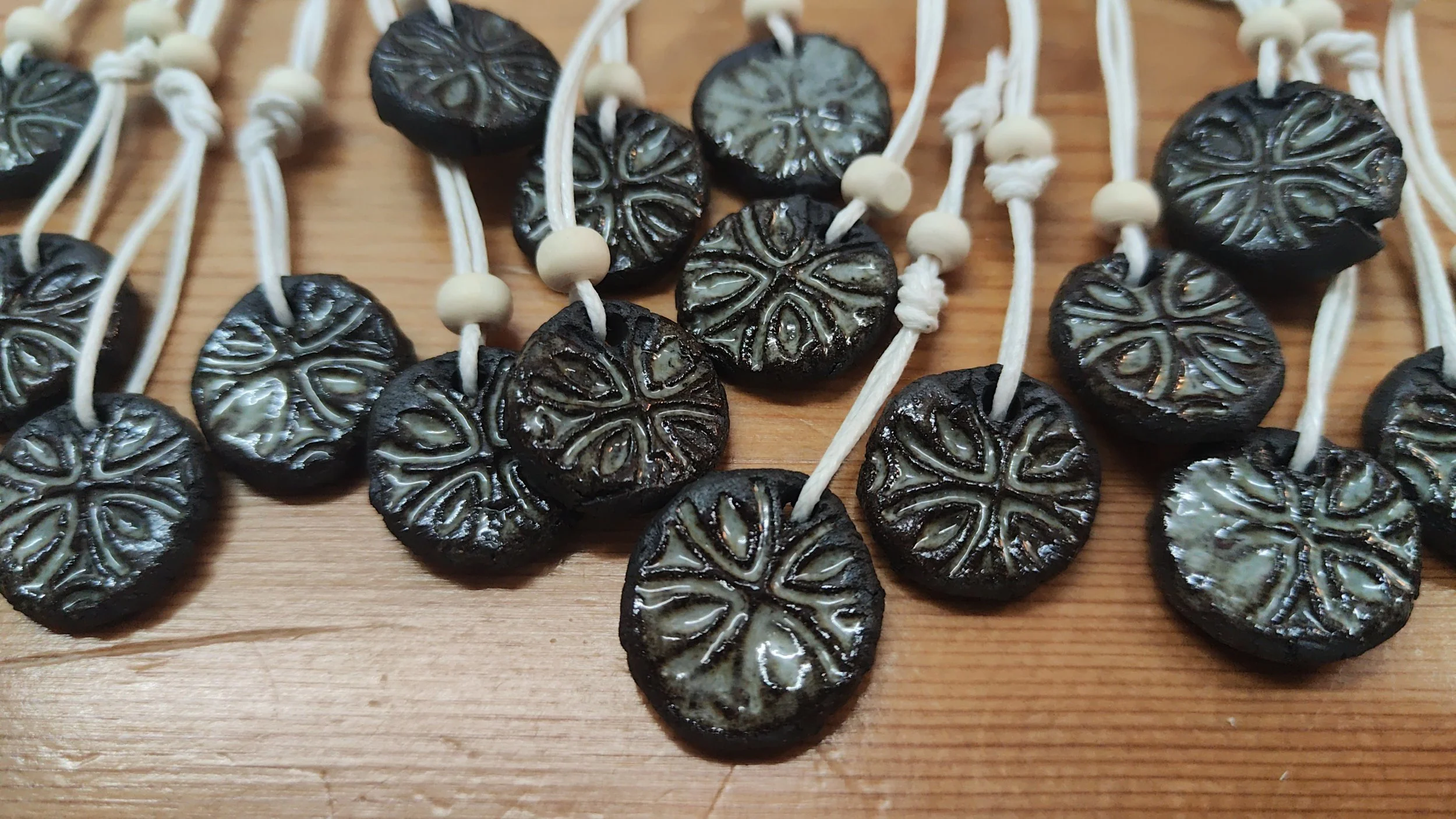 A close-up of several dark clay pendants with intricate white icing designs, arranged on a wooden surface.