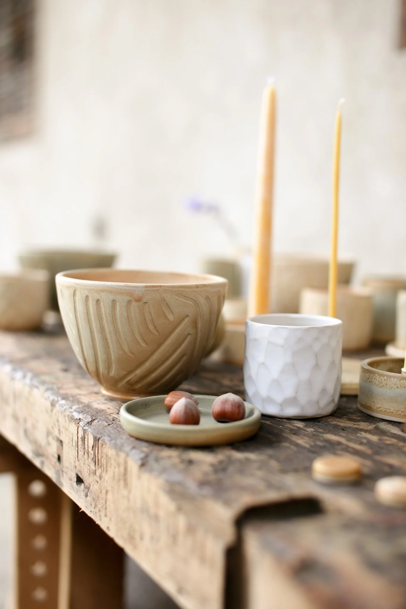 Various handmade ceramic bowls and cups with a textured white cup and a small dish with nuts, arranged on a rustic wooden surface.