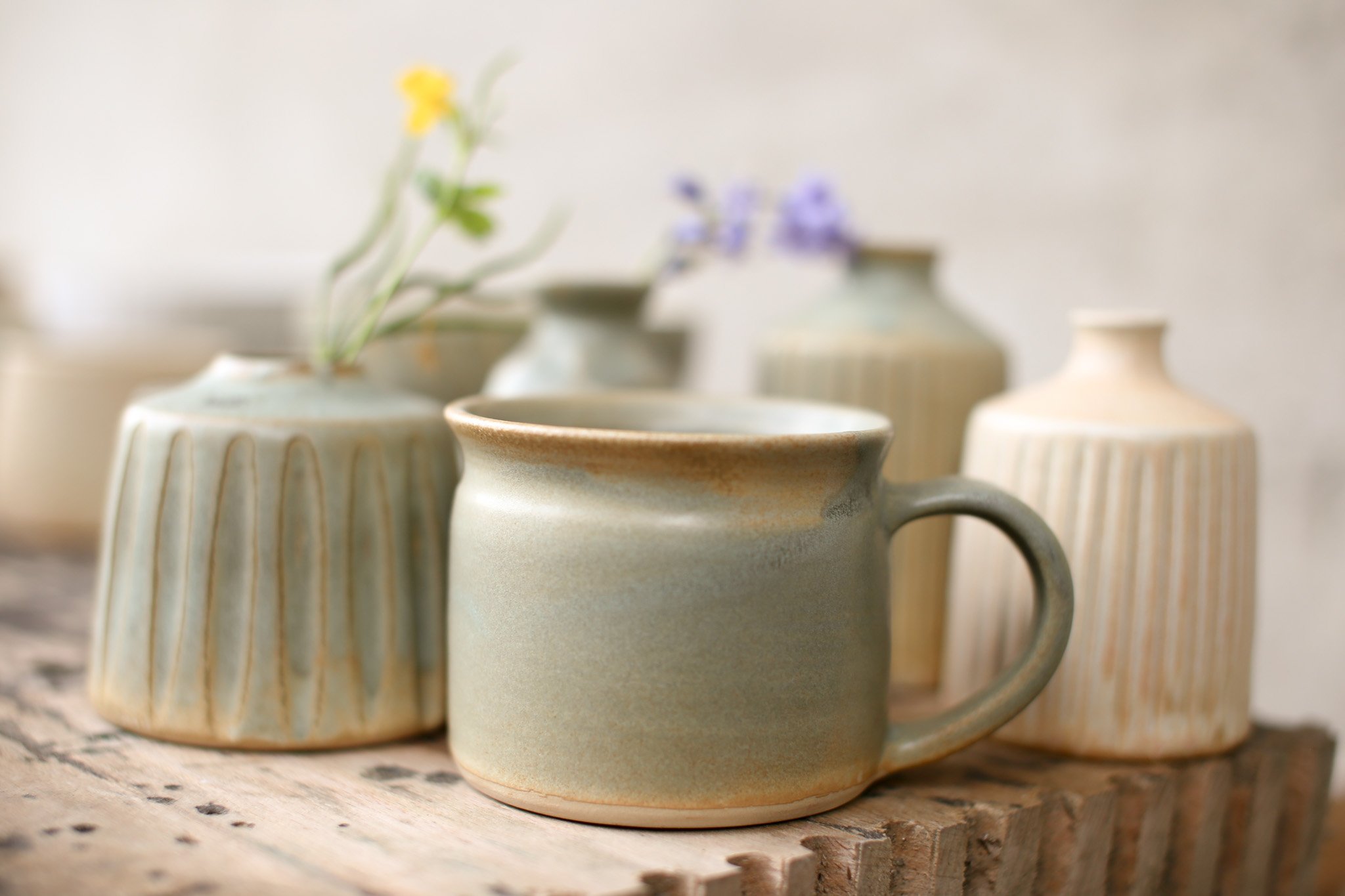 Several ceramic mugs with vertical striped patterns in earthy tones, placed on a wooden surface.