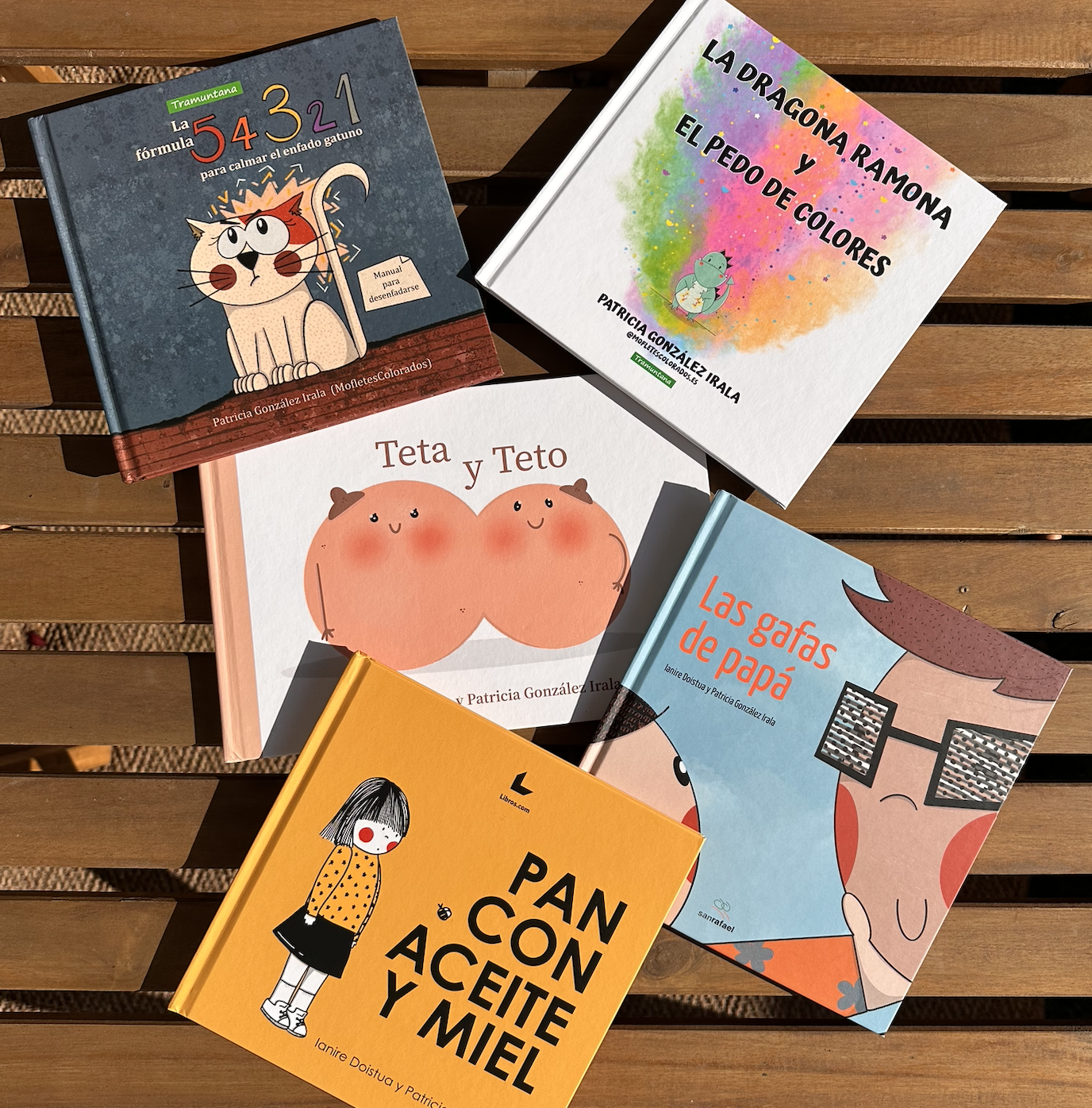 Colección de cinco libros para niños con ilustraciones coloridas. Títulos visibles: "La fórmula 54, 43, 321 para calmar el enfado gatuno", "La dragona Ramona y el peso de colores", "Teta y Teto", "Las gafas de papá", y "Pan con aceite y miel".