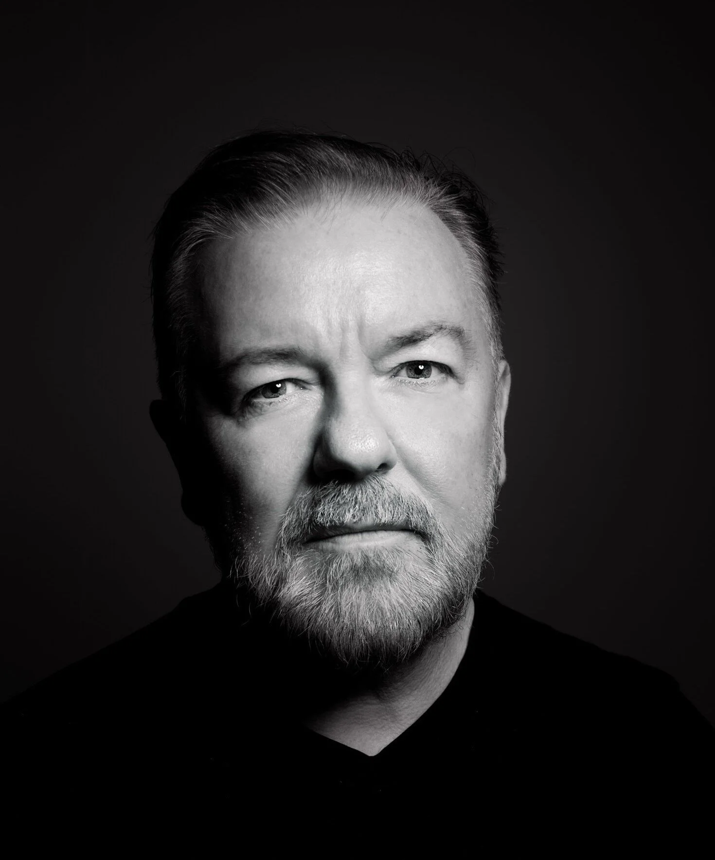 Black and white portrait of a middle-aged man with a beard and mustache, looking directly at the camera, against a dark background.
