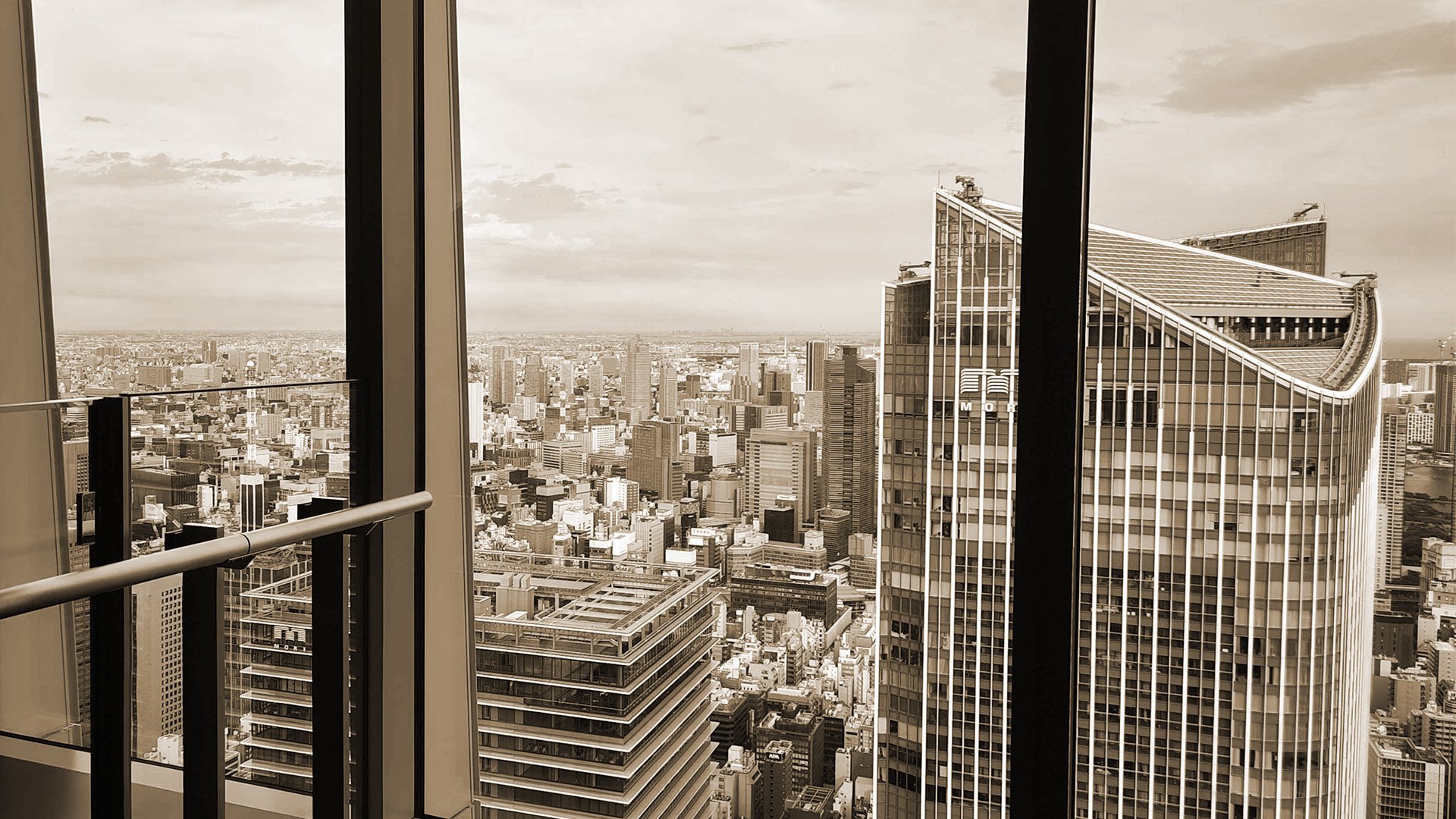 City skyline viewed from a high-rise balcony, showing tall modern buildings in black and white.