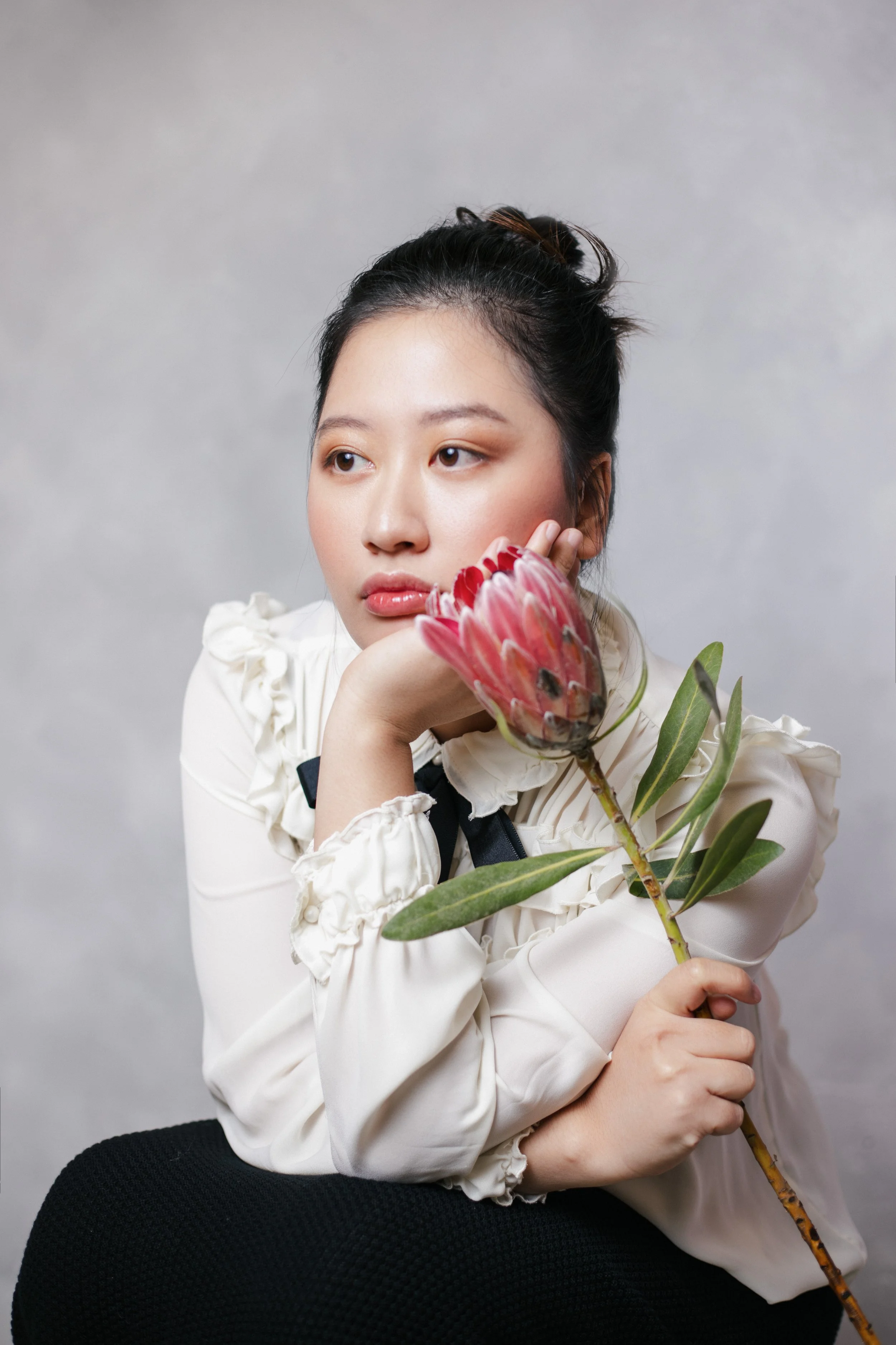 Portrait of Xuan Blooming, a children’s author and poet, holding a protea flower.