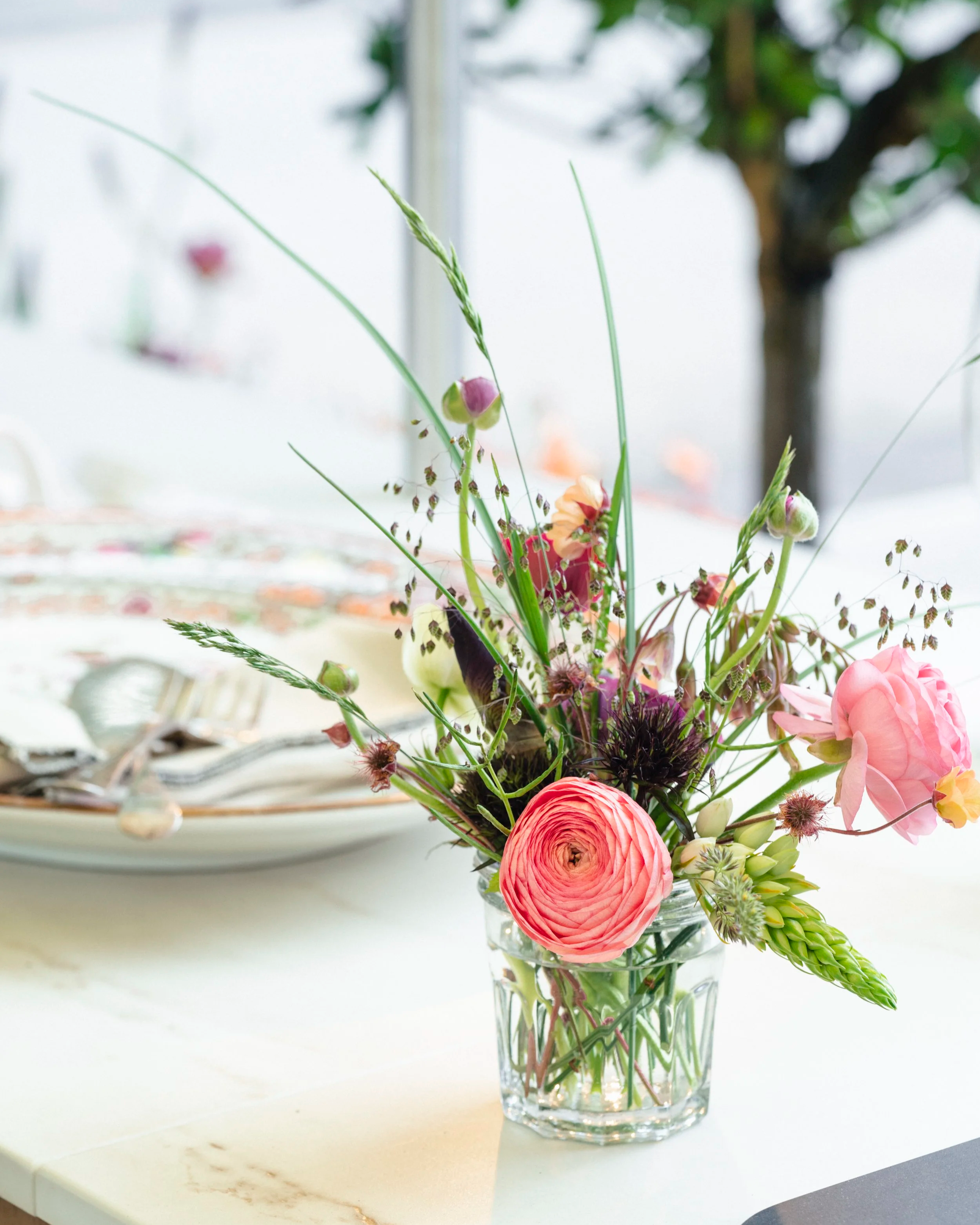 A bouquet of various flowers including pink, purple, and yellow blooms, arranged in a glass vase on a white marble surface.