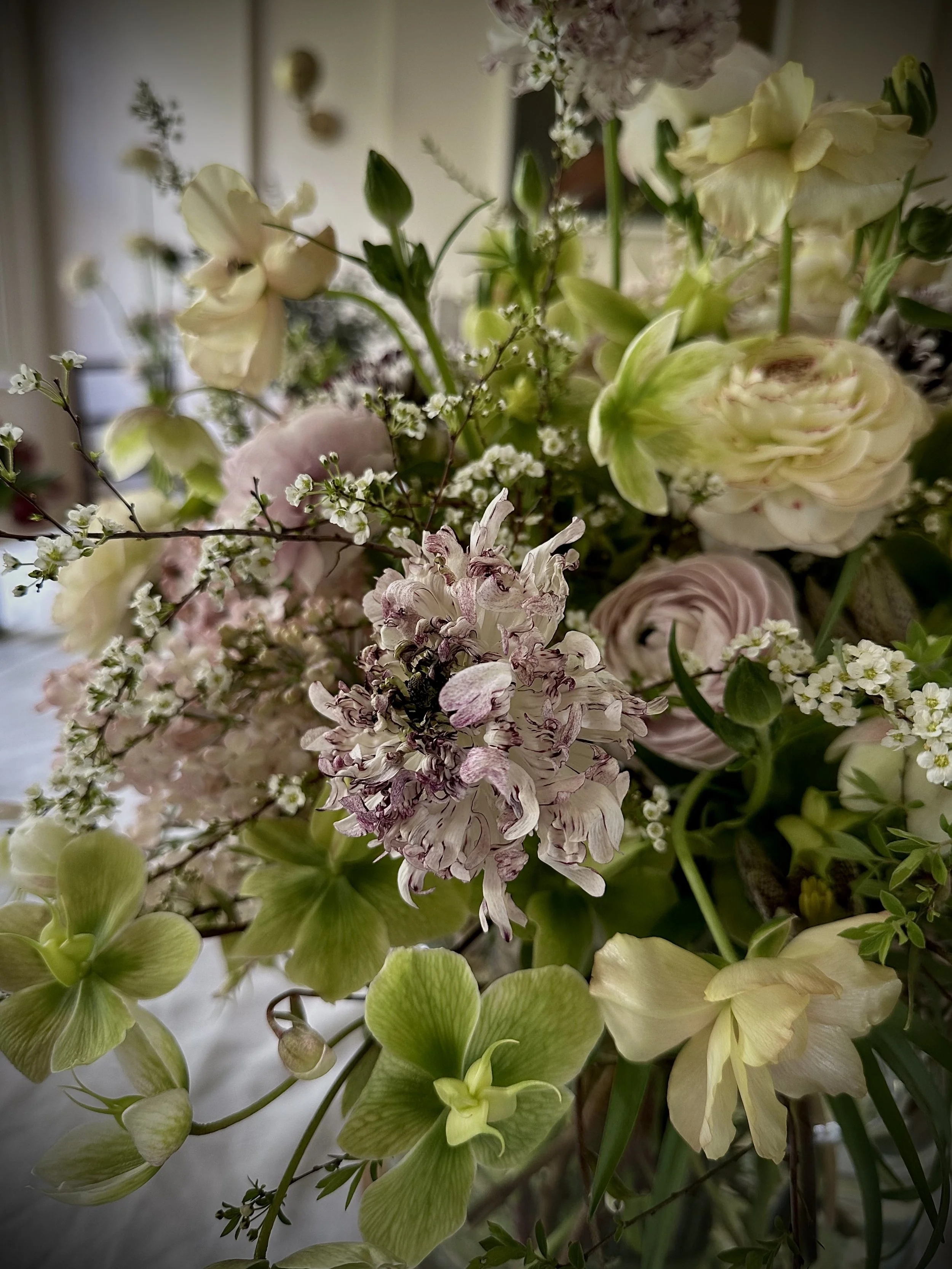 A close-up of a floral arrangement with white, pale yellow, and pink flowers, including hydrangeas, roses, and small white filler flowers.