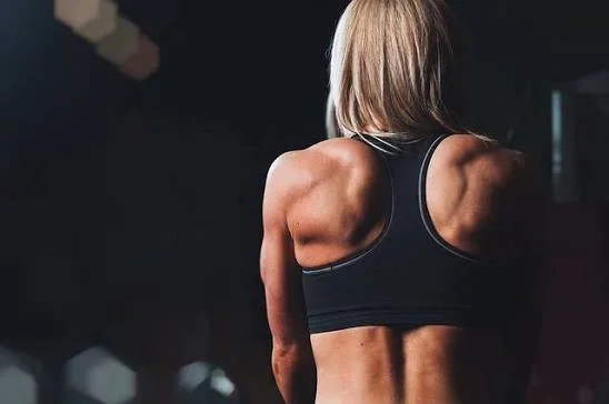 Back view of a woman with well-defined muscles in a dark gym setting.