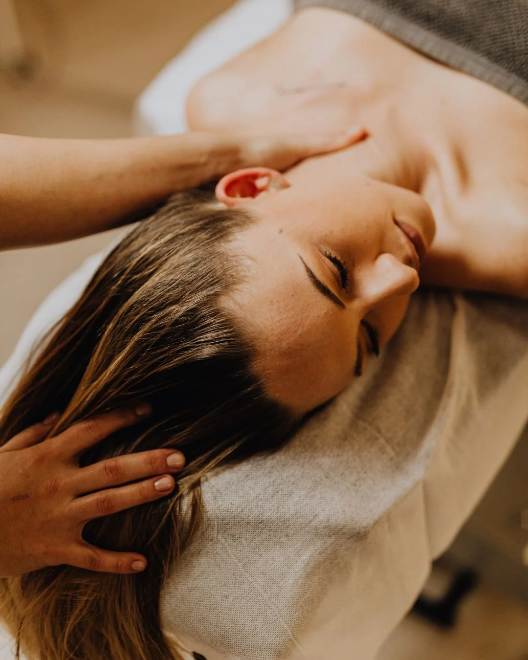 Une femme reçoit un massage relaxant, allongée sur une table avec un drap blanc. La scène est chaleureuse et calme.