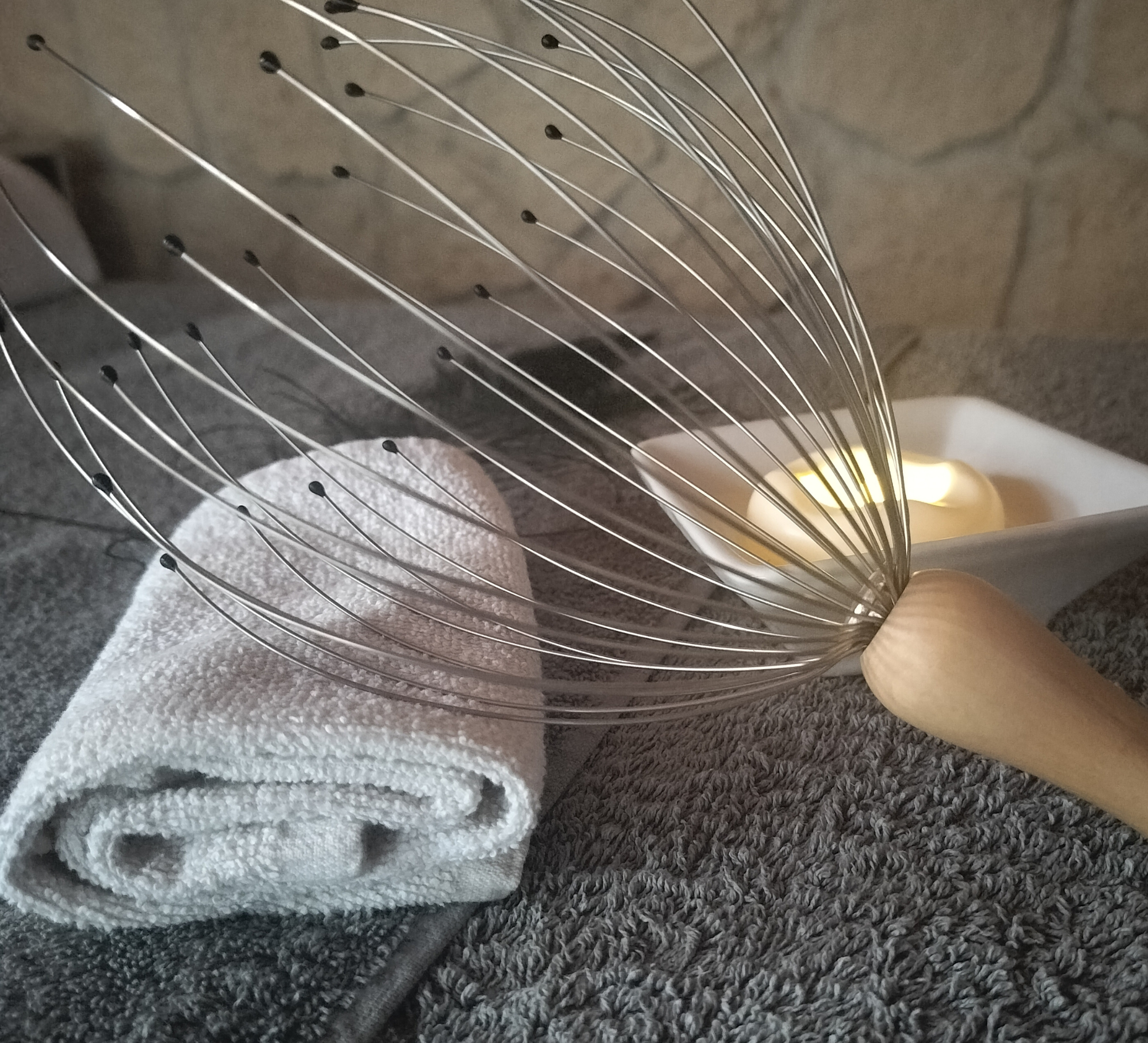 Ustensiles de cuisine : fouet en métal, serviettes blanches et grises en tissu, bougie dans un porte-candles blanc, fond de mur en pierre.