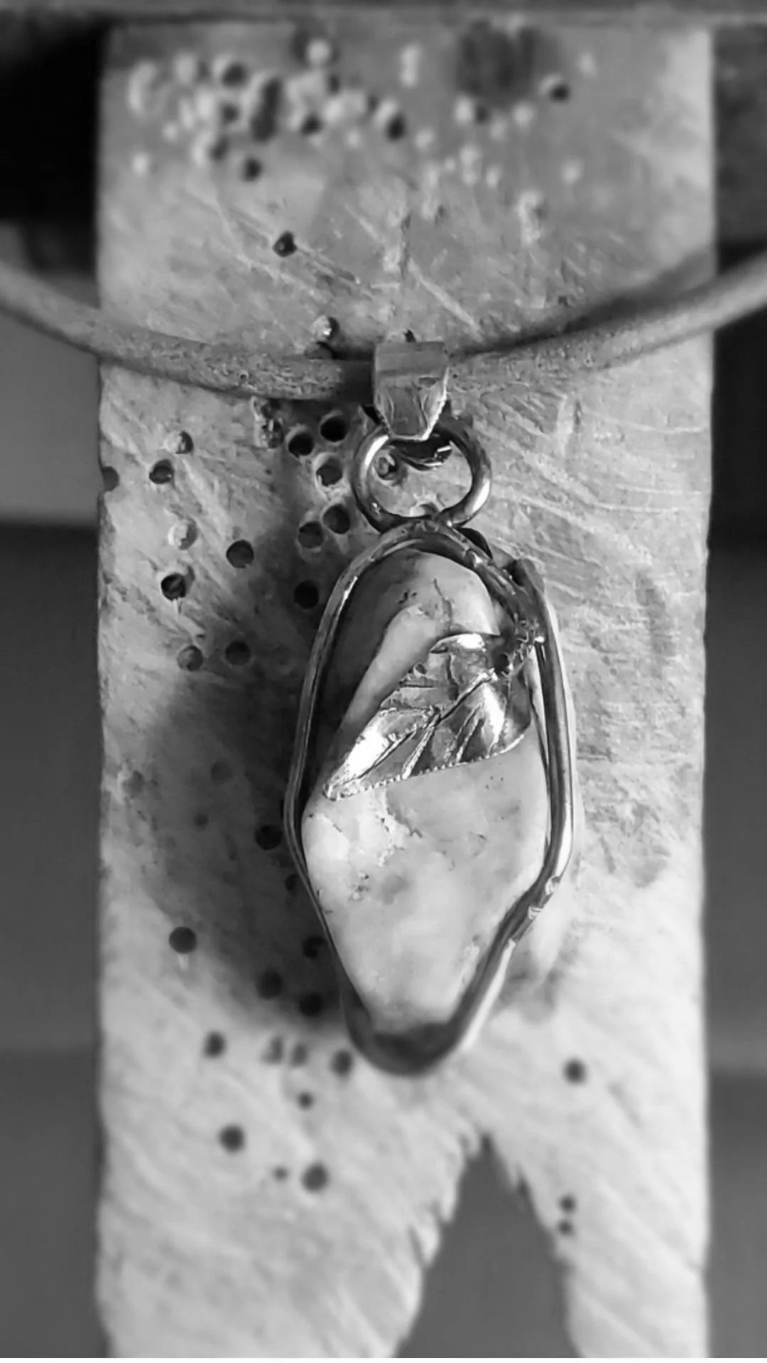 Pendentif en forme de nageoire de poisson avec pierre en verre, accroché à une chaîne, posé sur un dessus en pierre ou en béton.