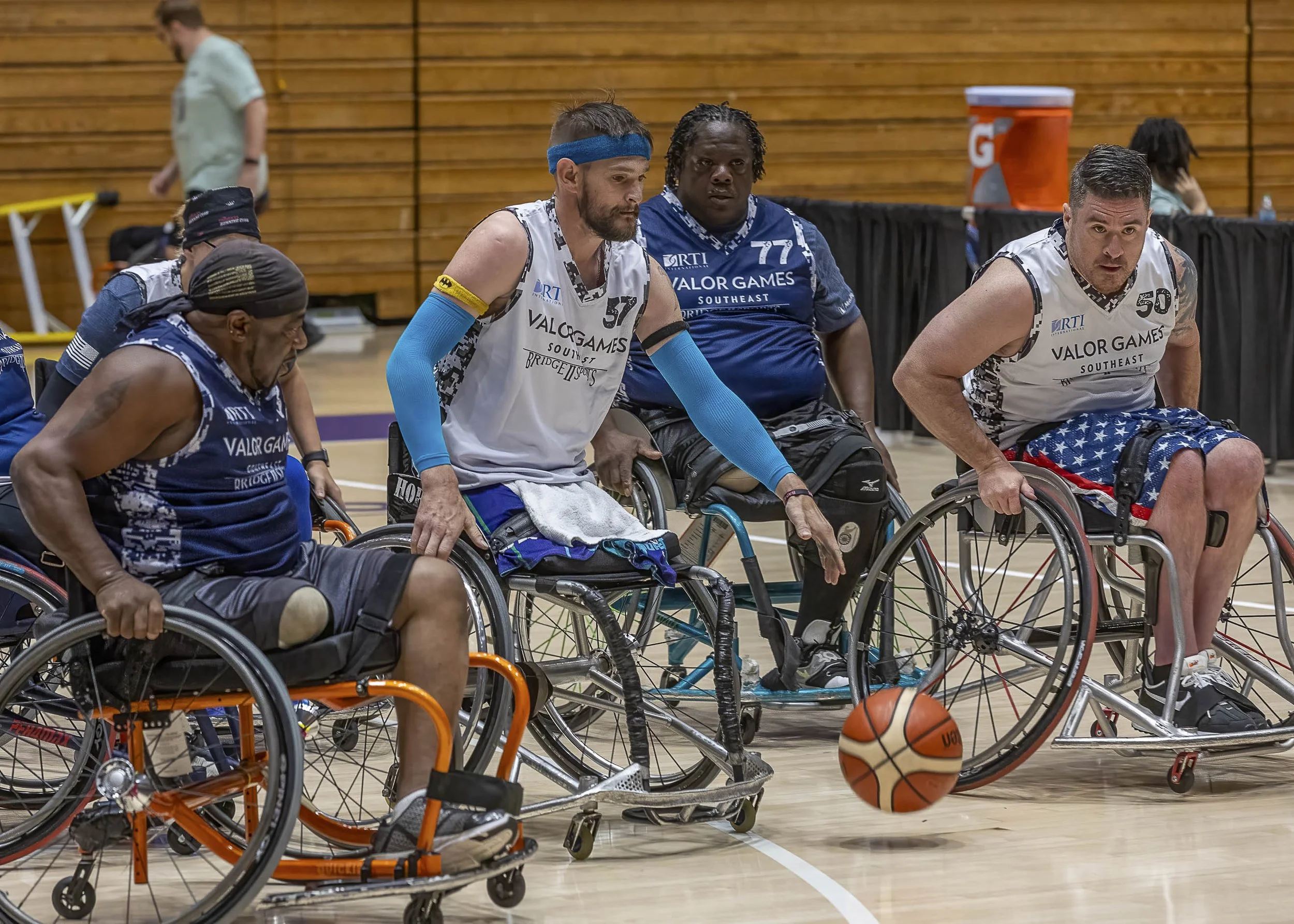 Wheelchair basketball players on court during a game, with the ball falling towards the ground.