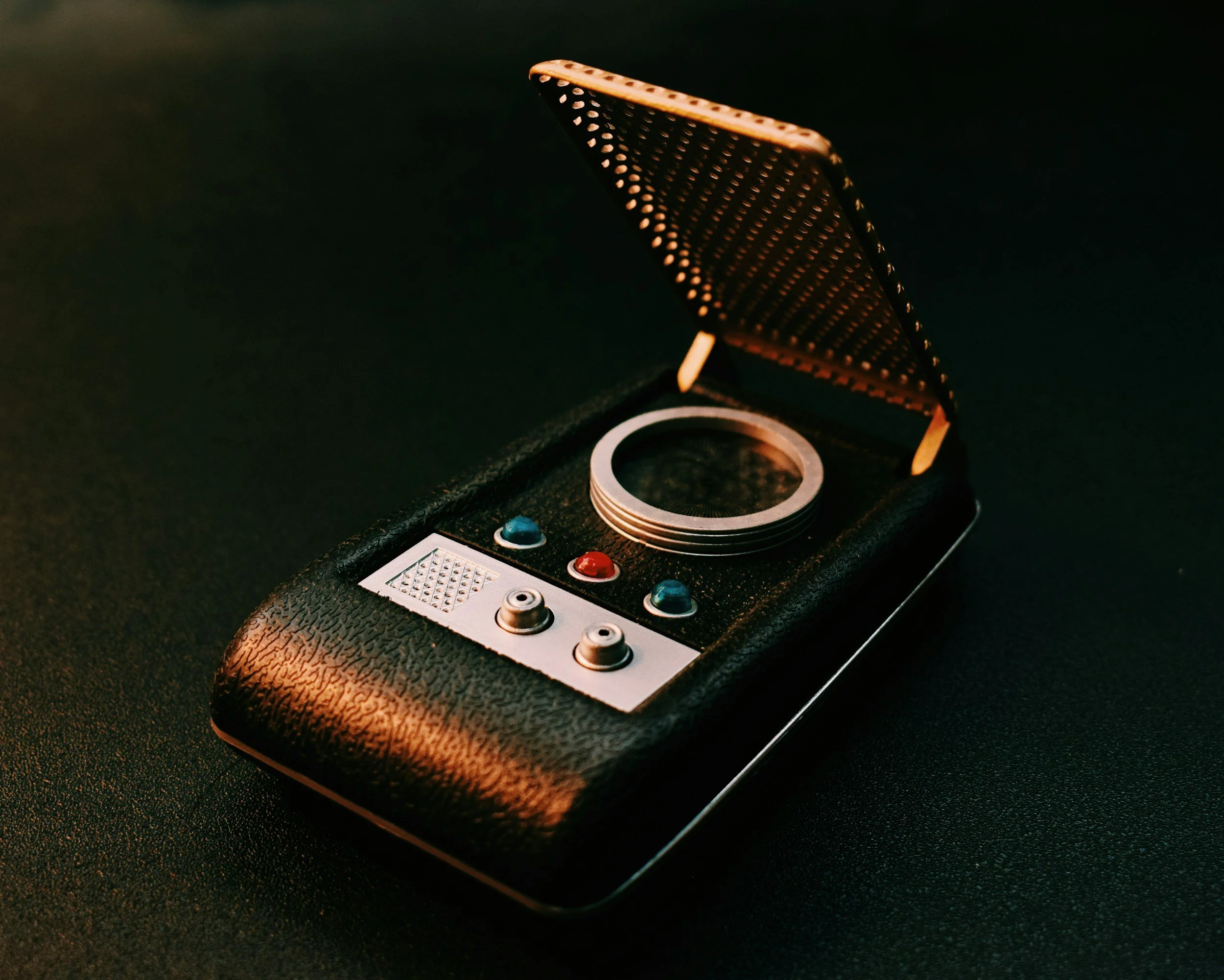 A vintage robot toy with a black textured body, red and blue buttons, and a circular screen, in an open black case with a gold interior.