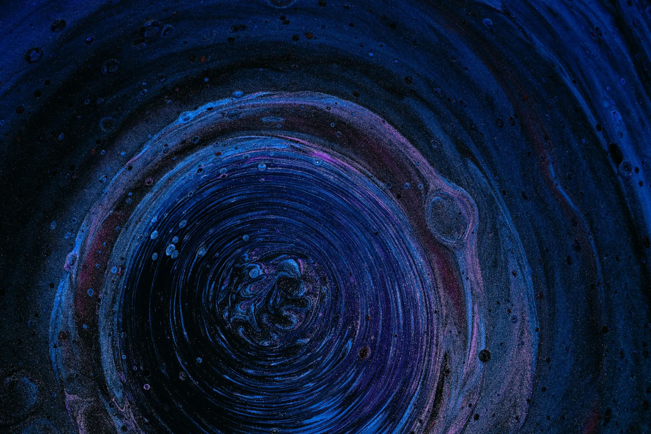 Close-up of a swirling vortex with shades of blue, purple, and black, resembling a cosmic or galaxy scene.