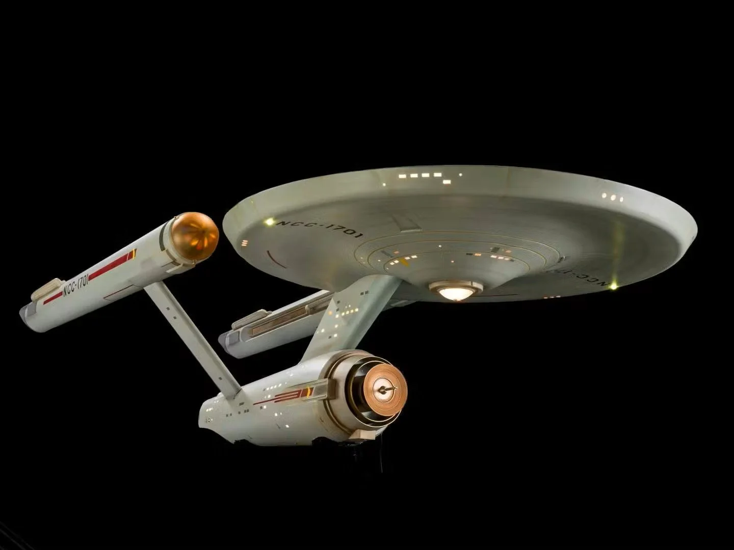 A detailed close-up of the USS Enterprise starship from Star Trek, floating in space against a black background, showing its saucer section, nacelles, and engineering section with illuminated details.