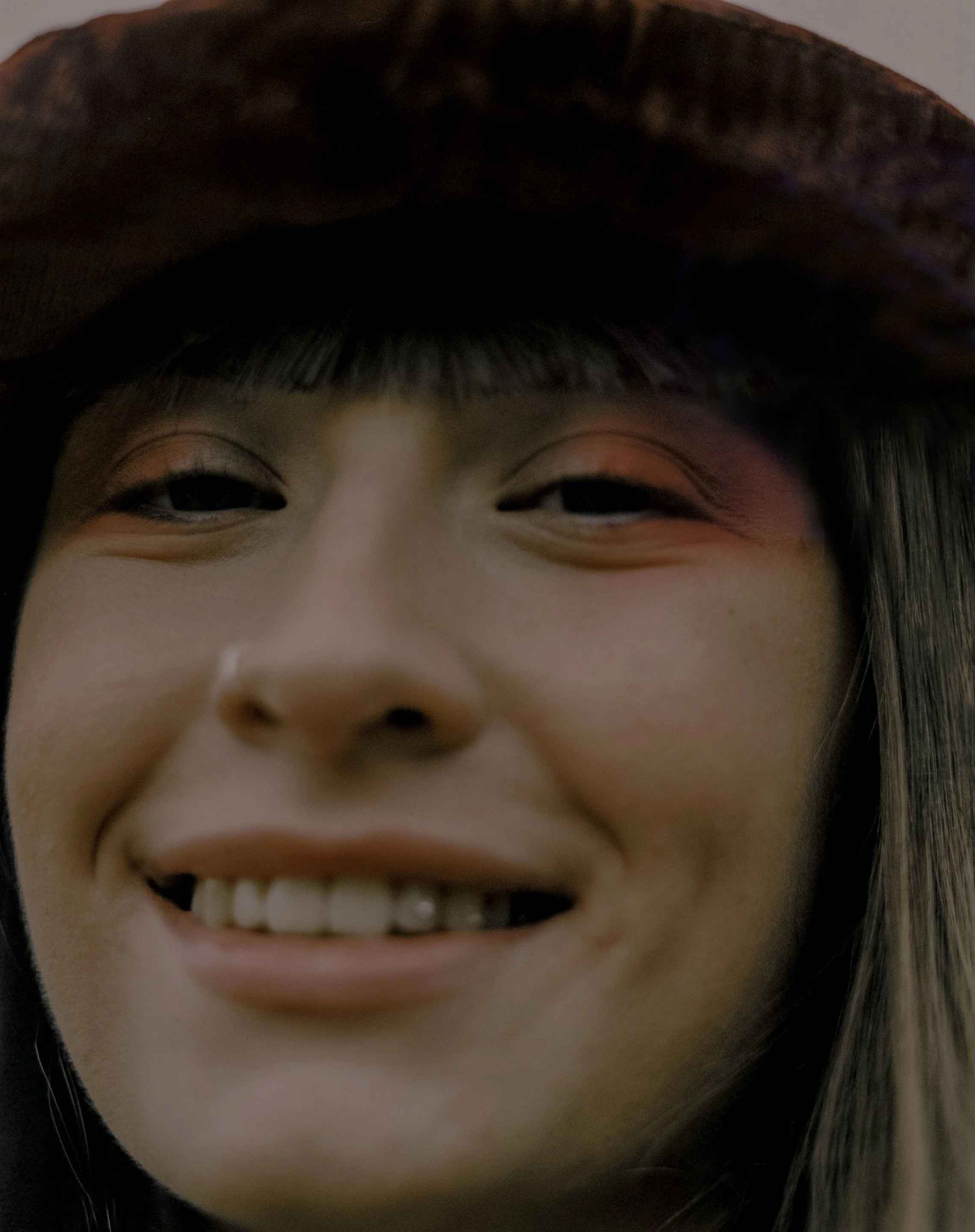 Close-up of a smiling woman wearing a brown hat and makeup with pink and purple eyeshadow.