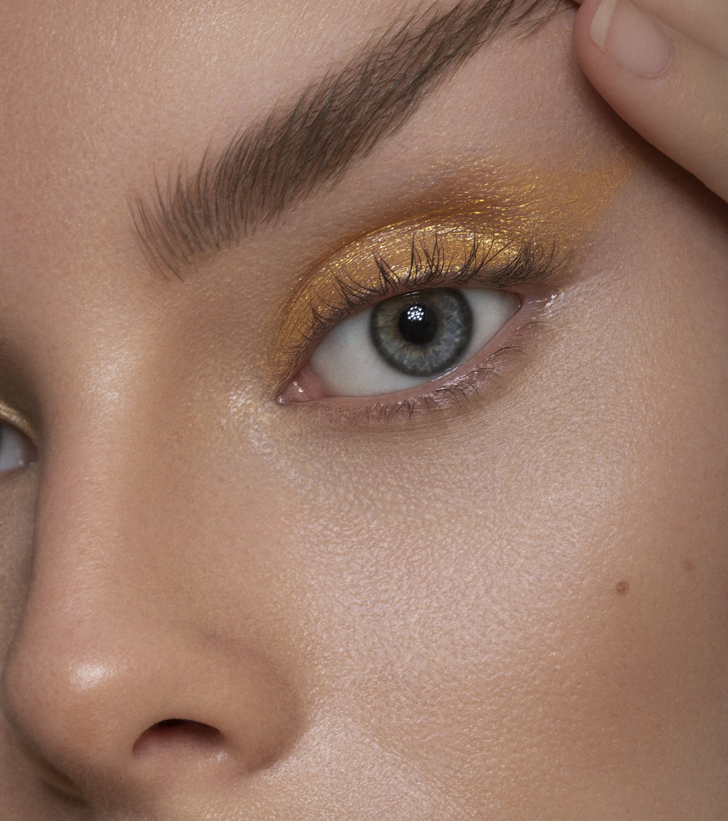 Close-up of a person's eye with gold eyeshadow and long eyelashes.