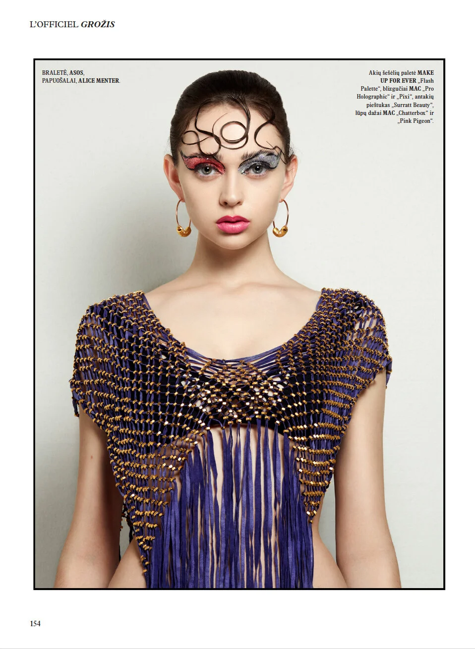Fashion model with elaborate makeup and accessories, wearing a purple and gold crochet top, gold hoop earrings, and featuring artistic eye makeup with red and silver glitter and curly hair embellishments.