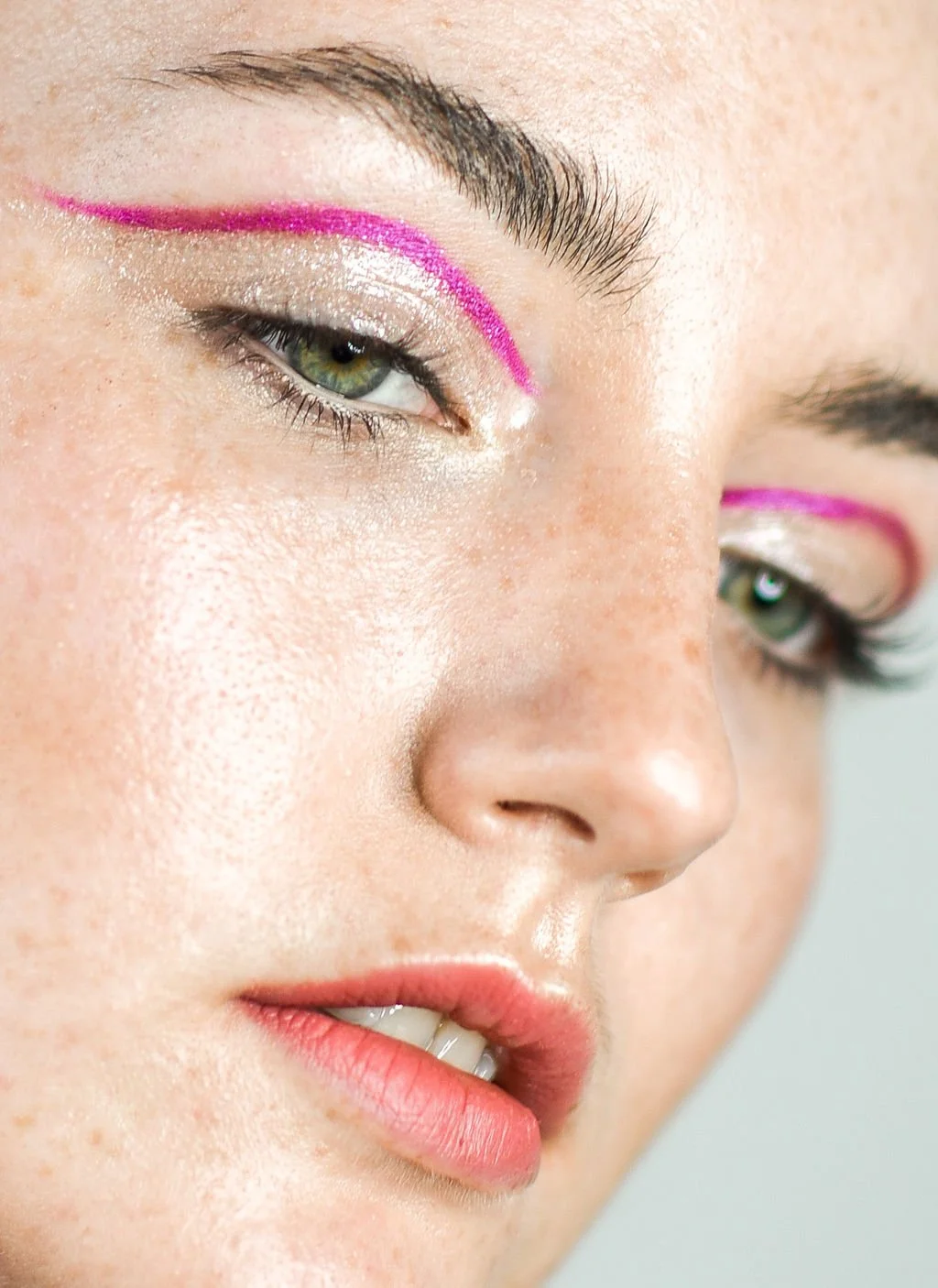Close-up of a woman's face focused on her eye area, featuring bold pink eyeliner, shimmery eyeshadow, and natural skin texture.