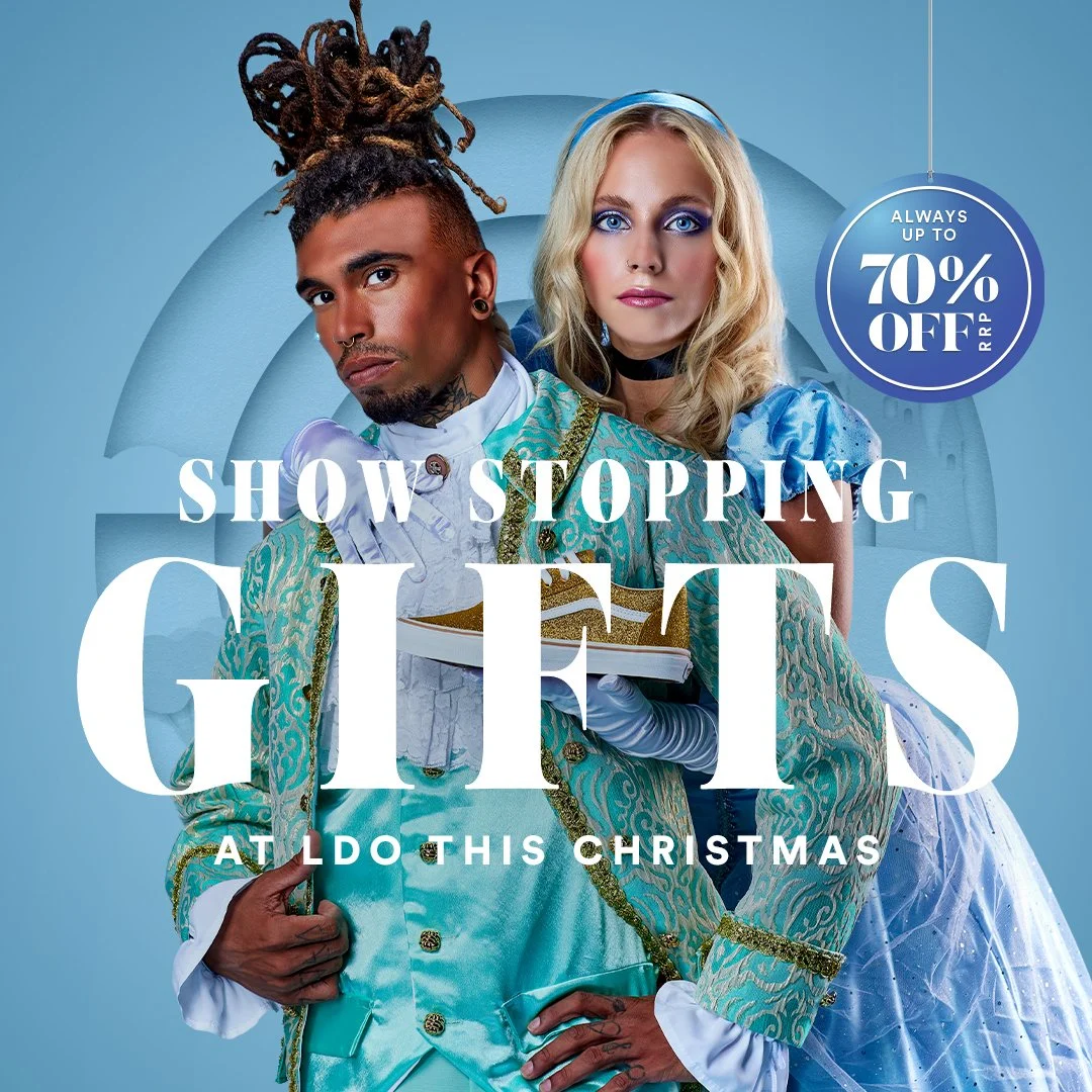 Poster for the show "Show Stopping Gays at Do This Christmas" featuring a man with dreadlocks and a woman with blonde hair. Both are in colorful, ornate costumes and looking at the camera. A blue background with a circular badge indicating "Up to 70%