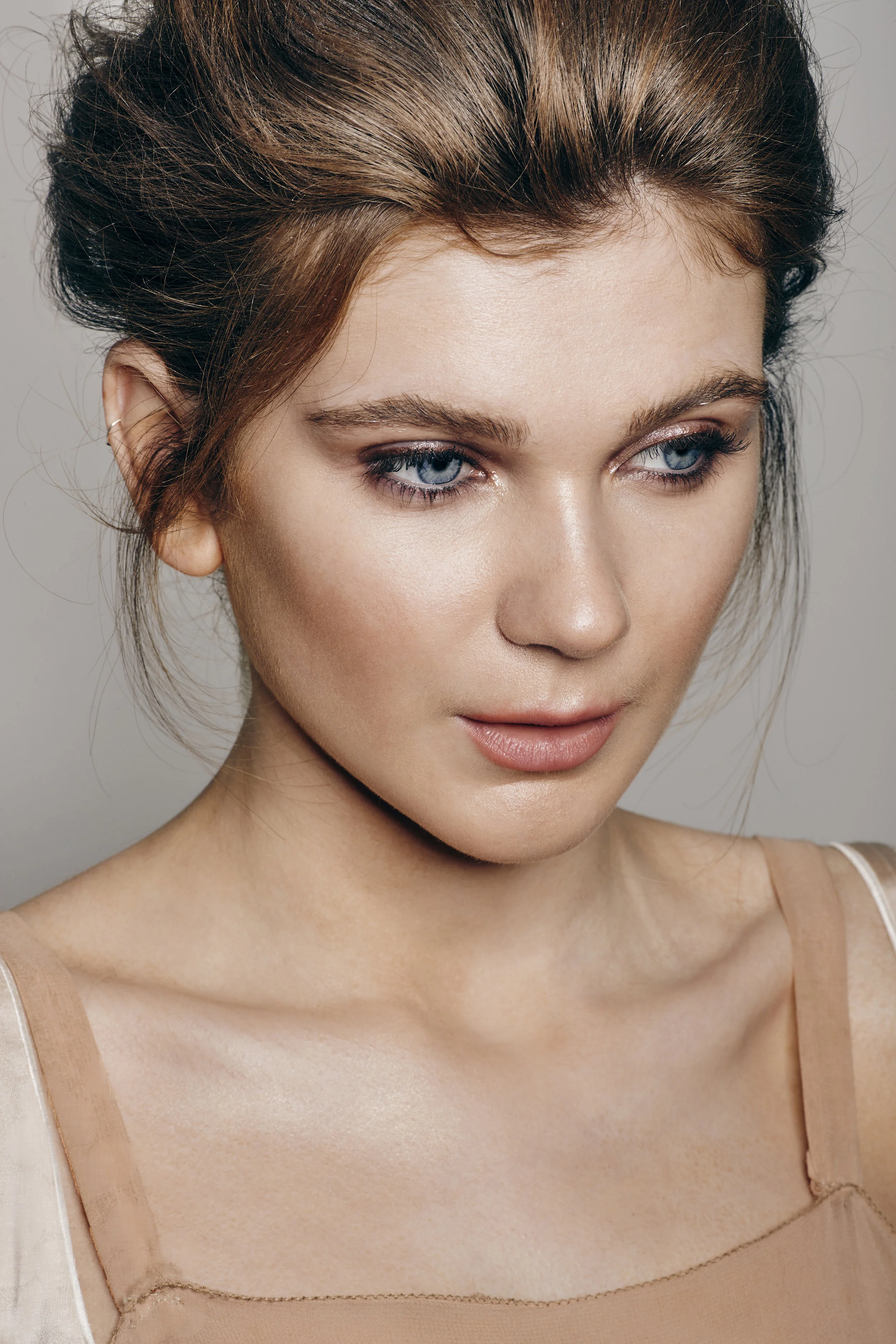 A woman with styled brown hair and blue eyes in a neutral top, looking slightly down.