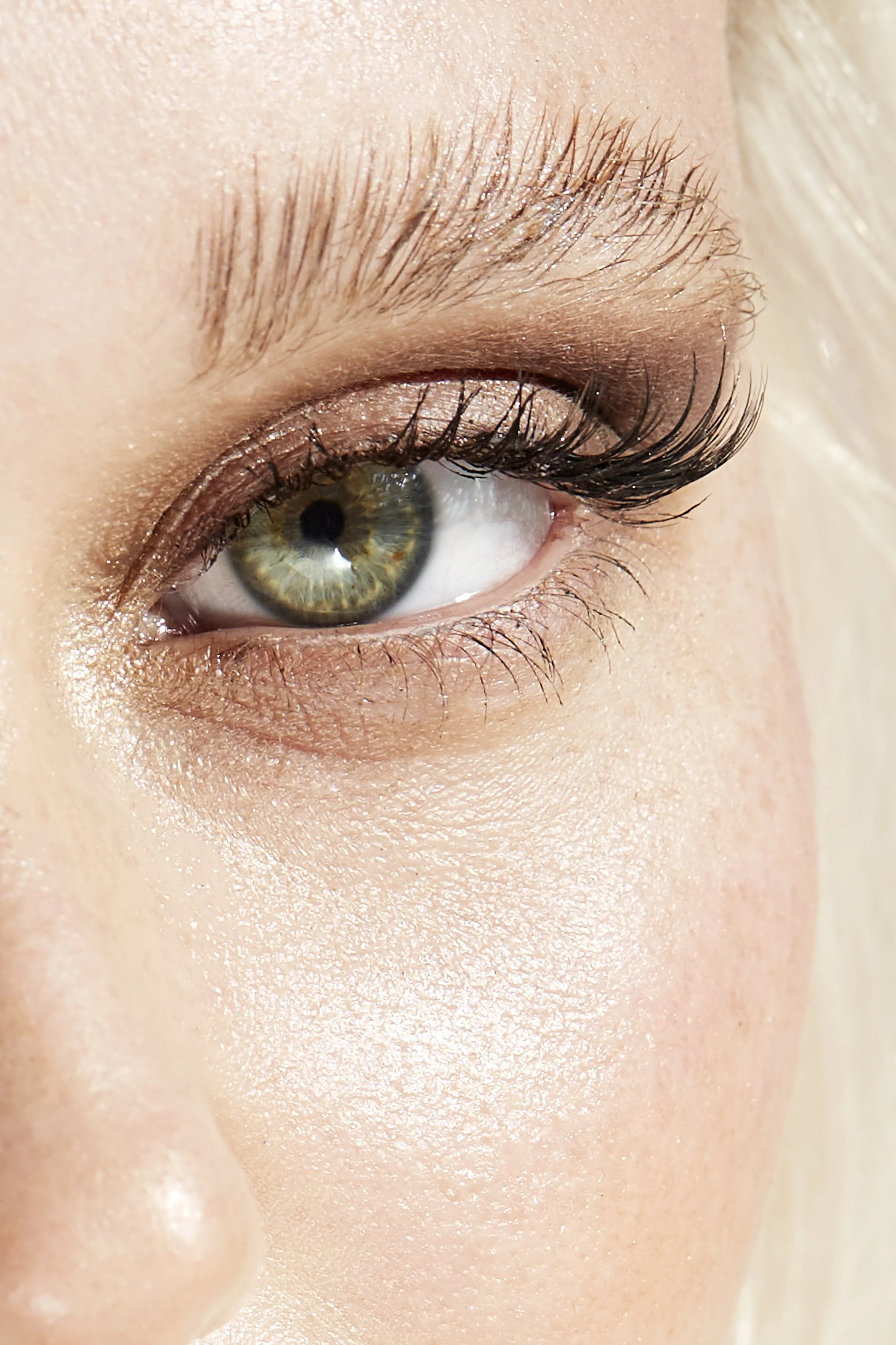 Close-up of a person's eye with green iris, makeup, and long eyelashes.