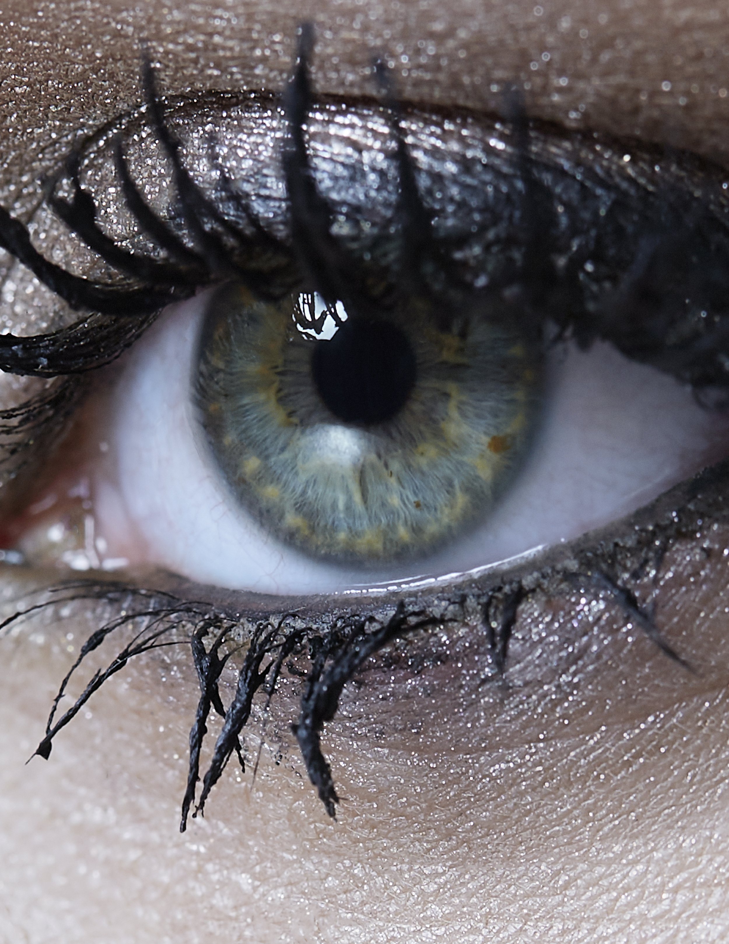 Close-up of a human eye with a greenish-gray iris and makeup, including black eyeliner and mascara, and wet eyelashes.