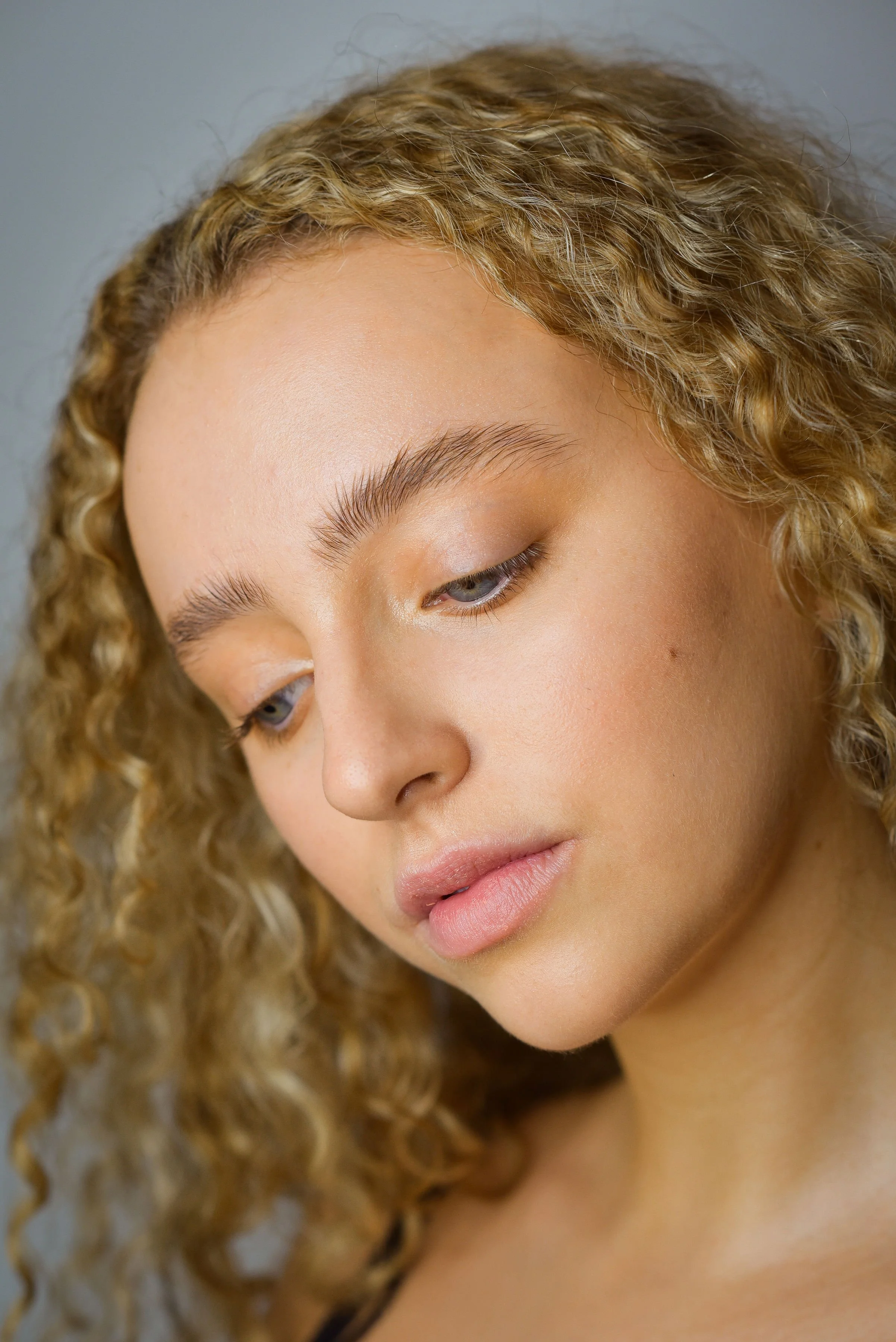 Close-up of a young woman with curly blonde hair, natural makeup, and a thoughtful expression.