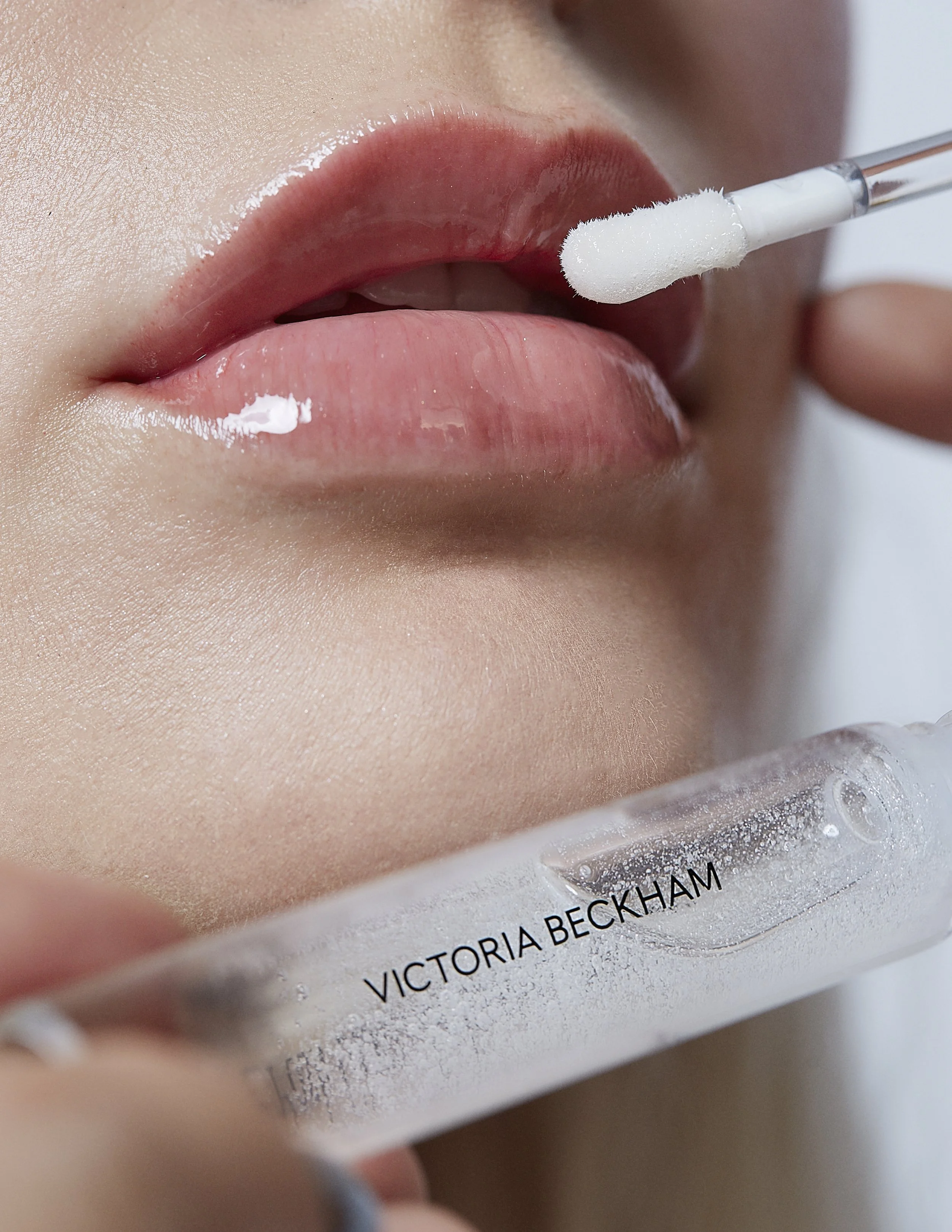 Close-up of a woman applying Victoria Beckham lipstick with a swab, showing her lips and part of her chin.