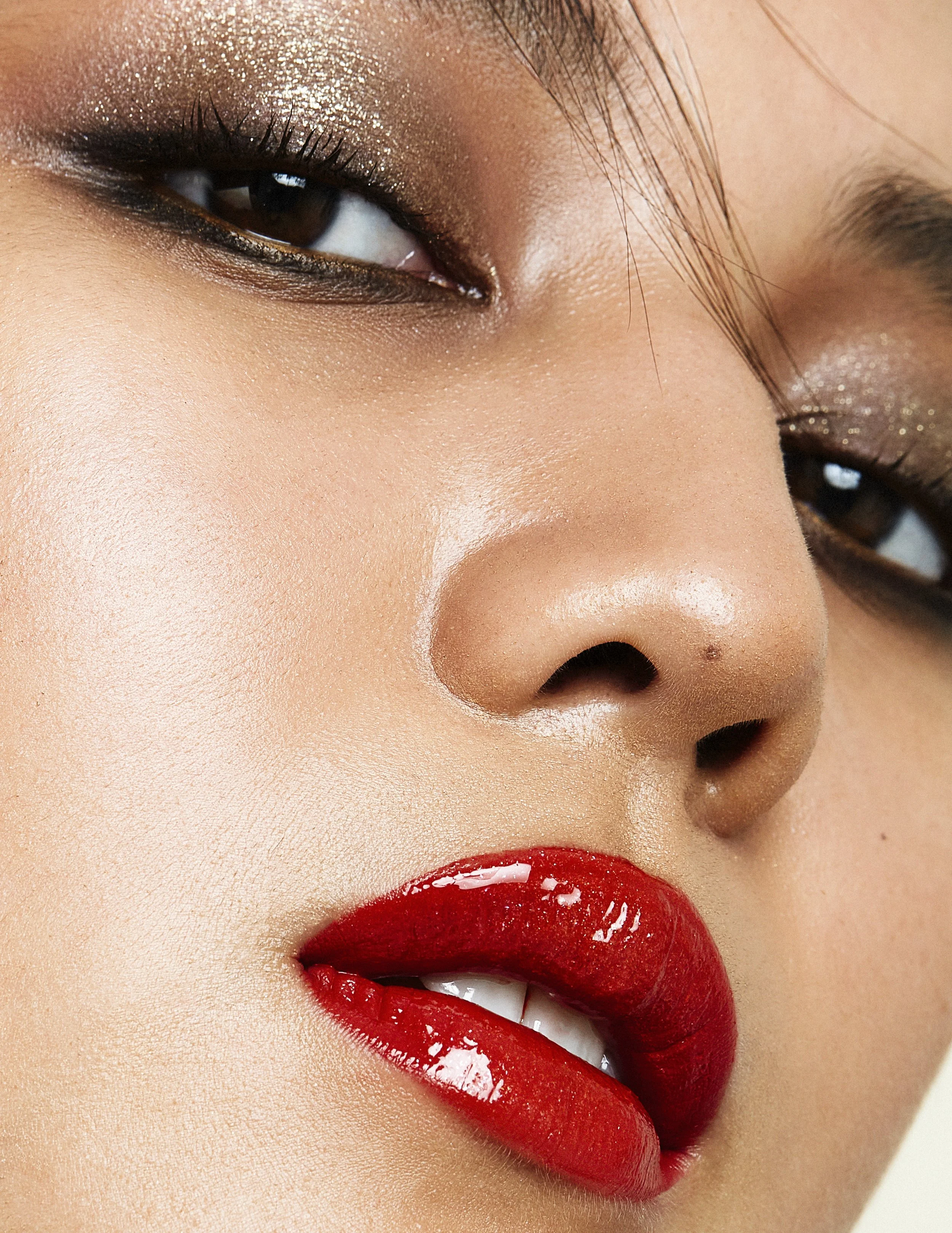 Close-up of a woman's face highlighting her eyes and lips, with glossy red lipstick and subtle eye makeup.