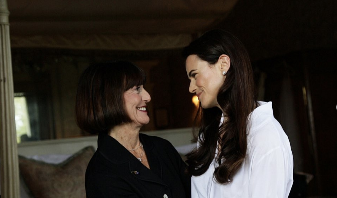 Two women smiling and looking at each other in an indoor setting.