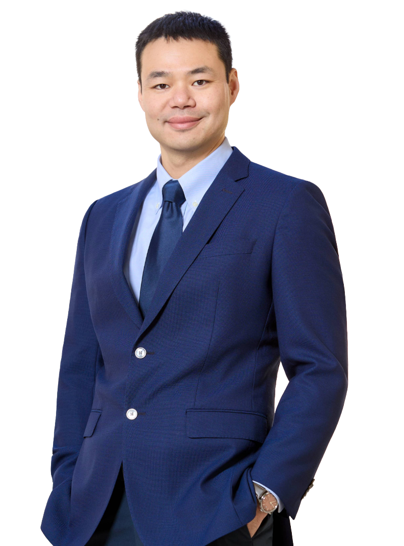 Portrait of a man in a blue suit, light blue dress shirt, and blue tie, smiling and standing with his hands in his pockets.