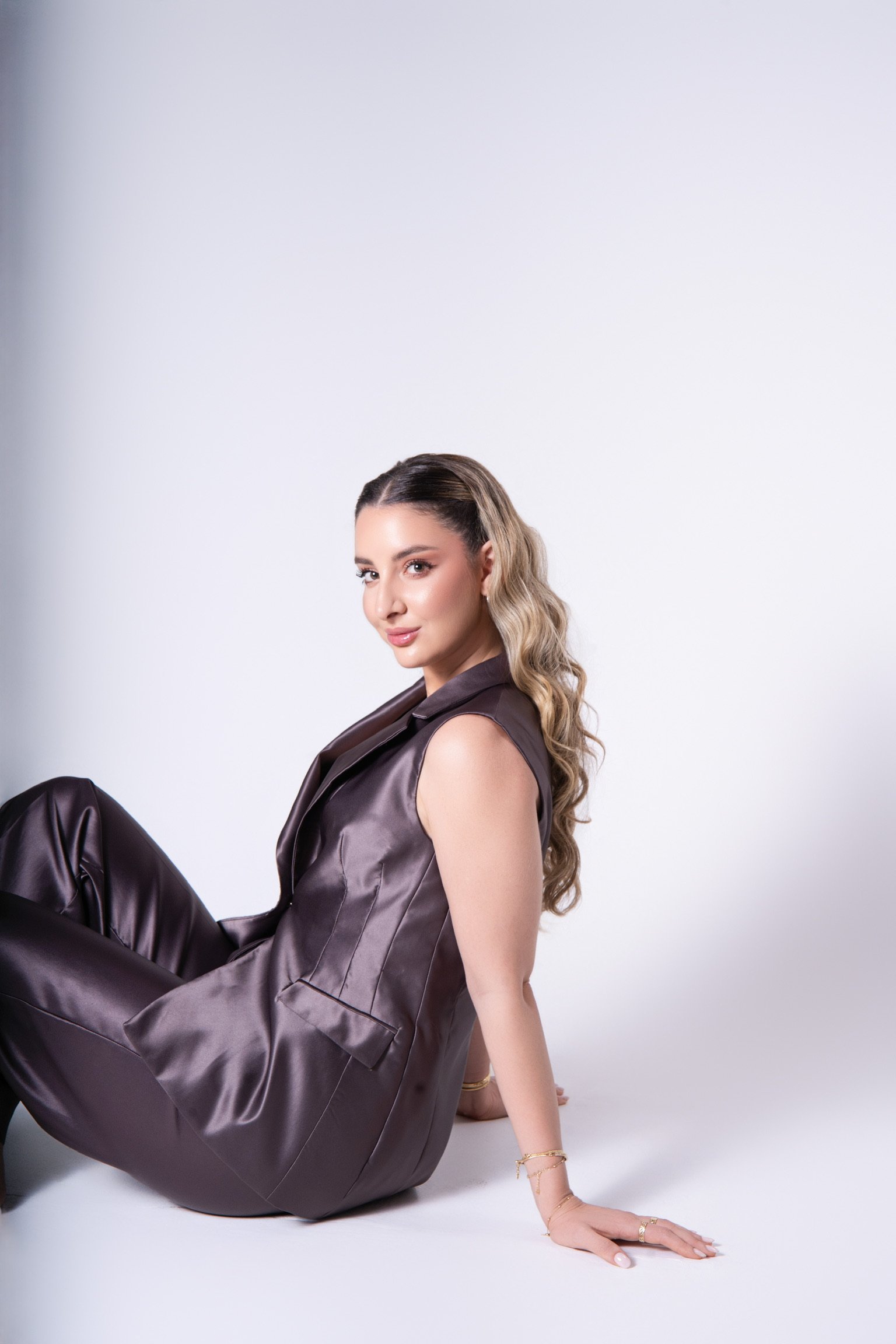 Mujer sentada en el suelo con vestimenta de satín y cabello rizado.