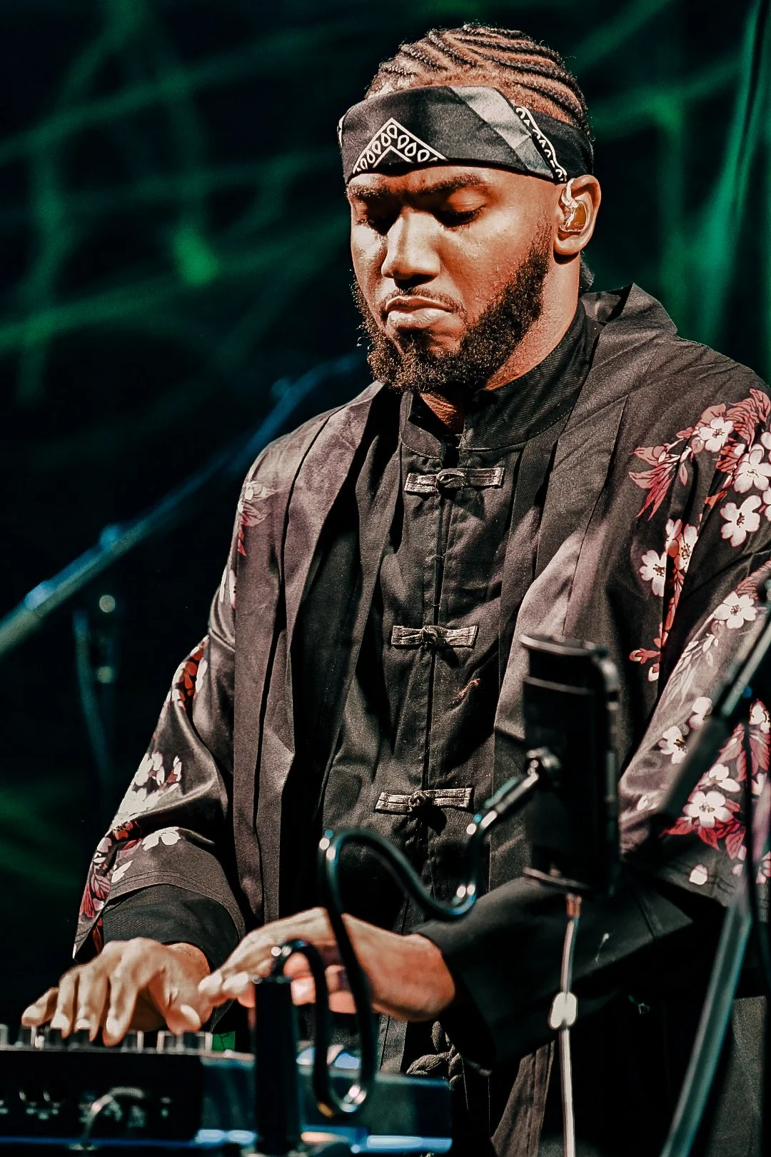 A male DJ or music producer is performing with equipment in a dark setting with green lighting background.