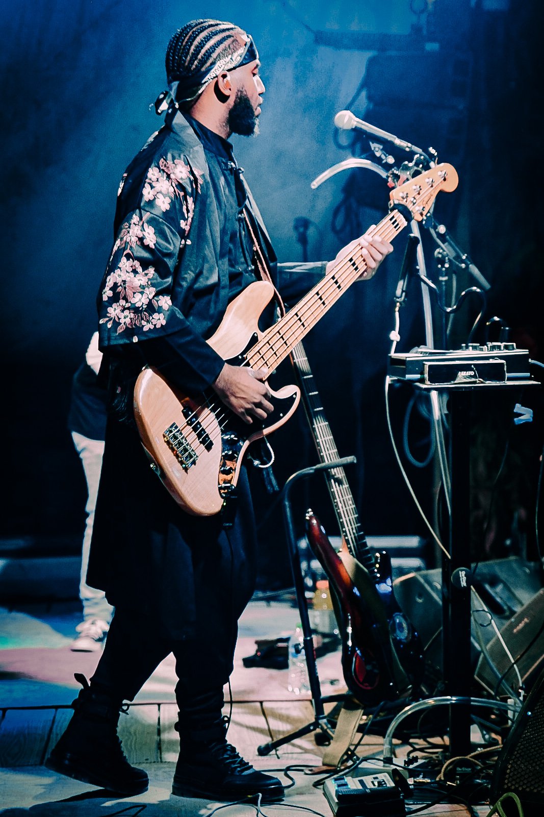 Musician playing a bass guitar on stage with a microphone and sound equipment.
