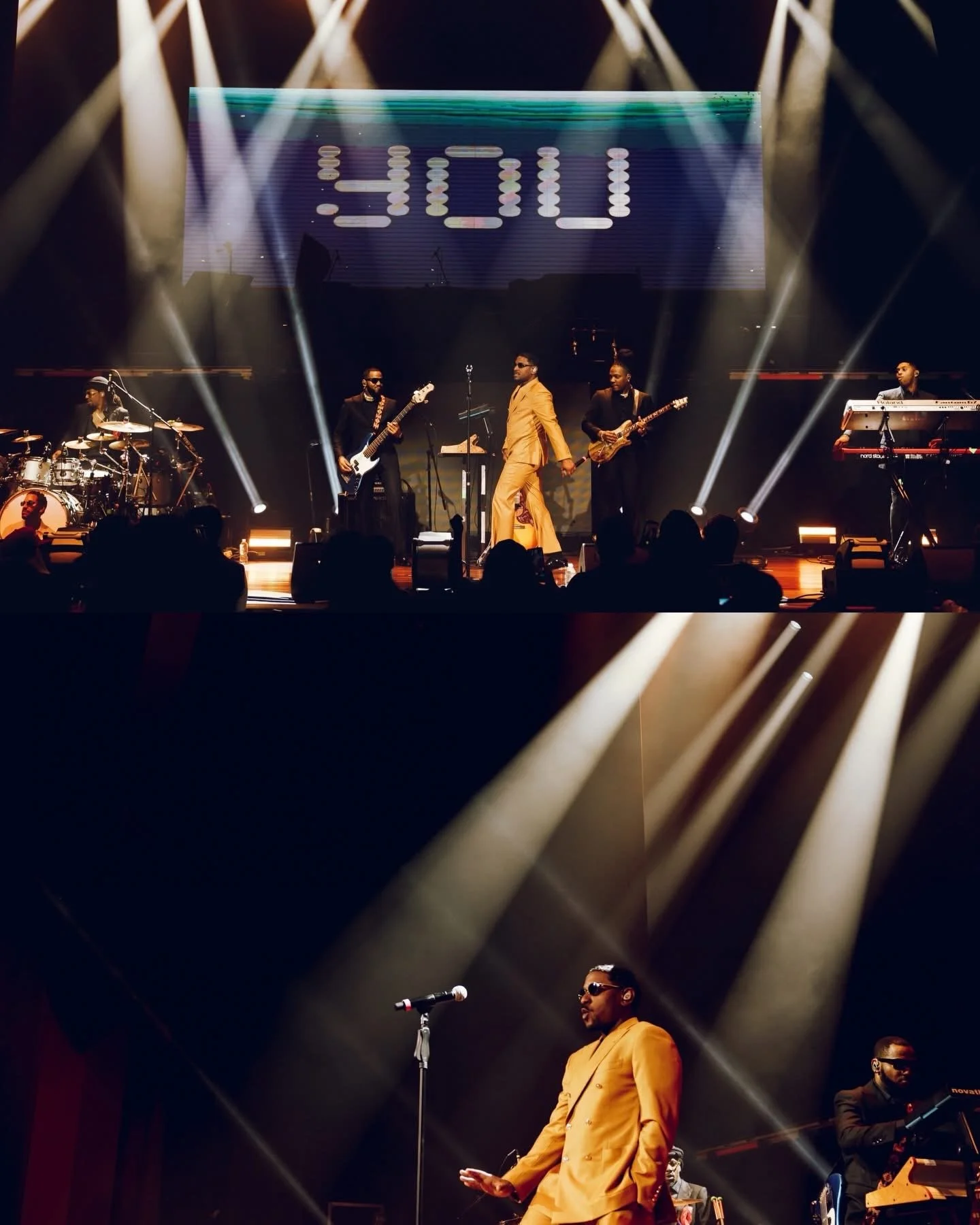 A musical performance on stage with a man in a yellow suit singing and holding a microphone, band members playing instruments, and stage lights with a digital display showing the number '410' in the background.