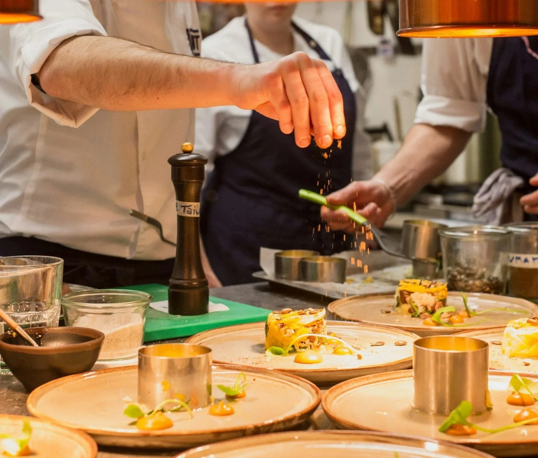 Chefs garnishing plated dishes with herbs and spices in a professional kitchen.