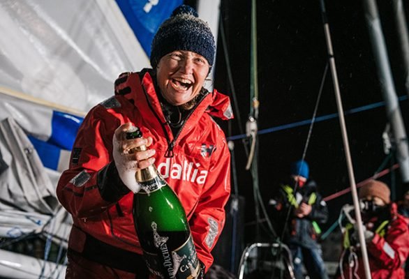 Pip Hare Ocean Racing sailor celebrating with a bottle of champagne on board a sailboat at night, at Vendee Globe finish.