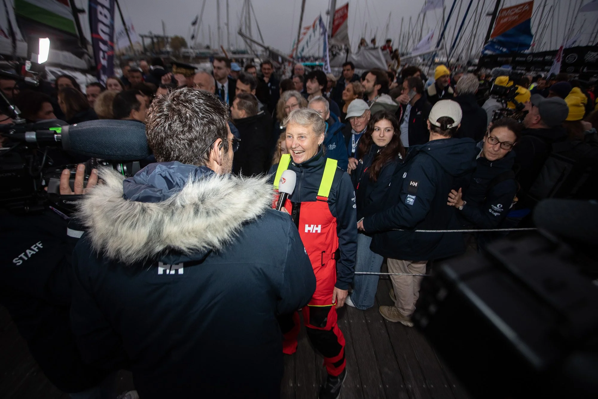 Pip Hare Ocean Racing - sailor in red sailing gear being interviewed at a busy marina at the Vendee Glove finish sailing event.