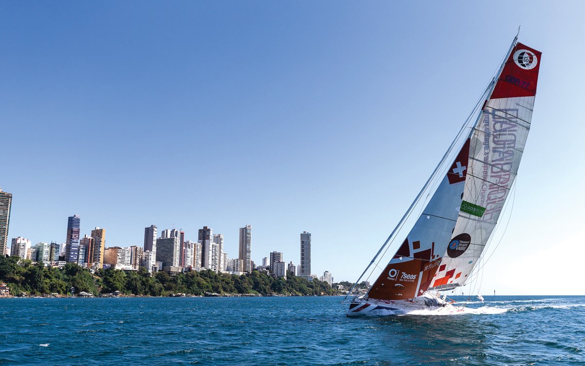 Pip Hare Ocean Racing racing yacht sailing near a city skyline on a clear day.