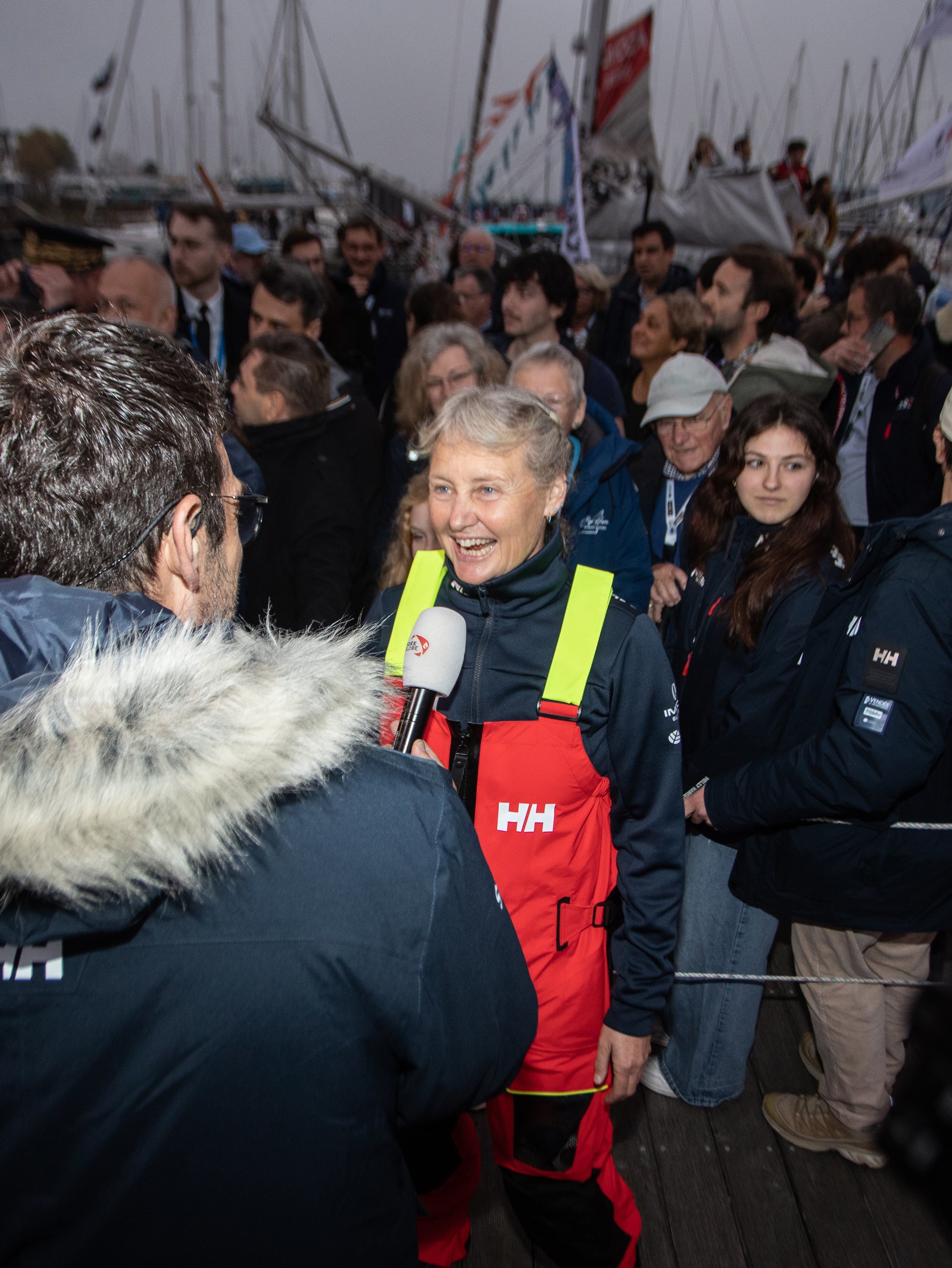Pip Hare Ocean Racing - sailor in red sailing gear being interviewed at a busy marina at the Vendee Glove finish sailing event.